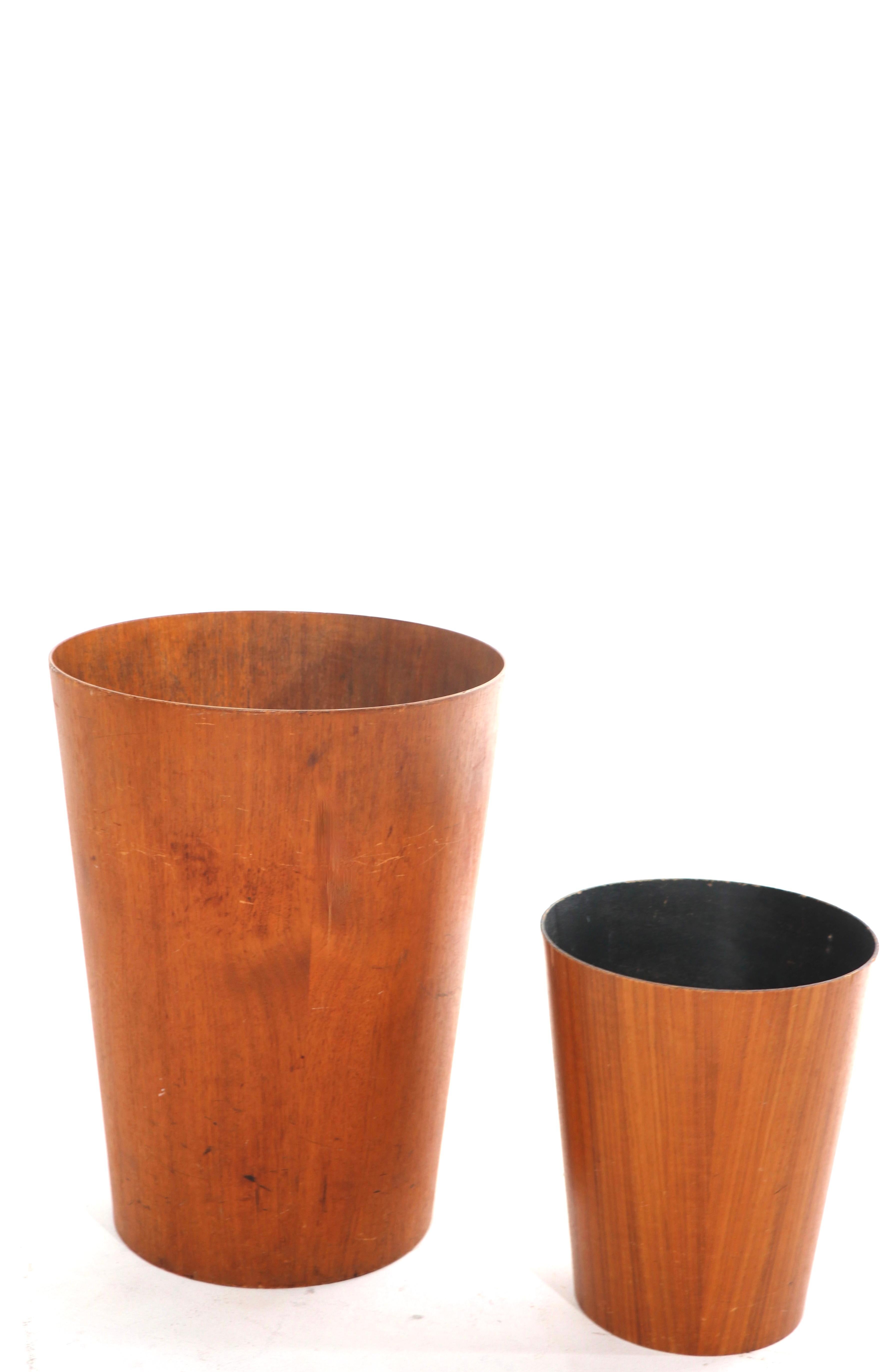 Unusual large scale teak trash can, shown next to a standard size version. This lot includes only the larger trash bin pictured. This example has some condition issues, specifically, a bruised at the bottom and non structural split in the body.