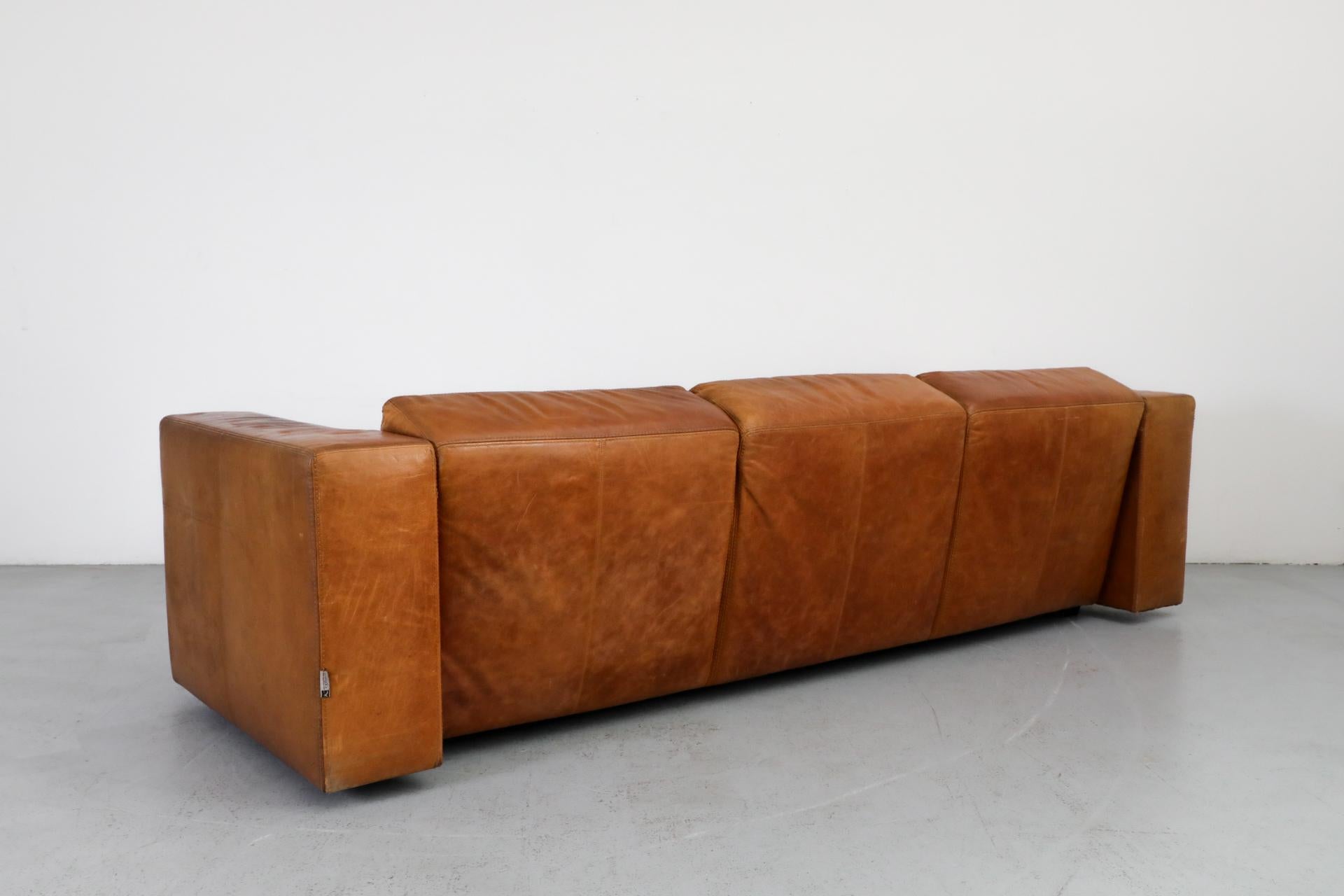 Massive Gerard van den Berg style cognac leather sofa by Topform. Over 9 ft long, with original cognac leather with heavy patina, and wide almost table like arm rests. In good original condition with beautiful patina and visible wear consistent with