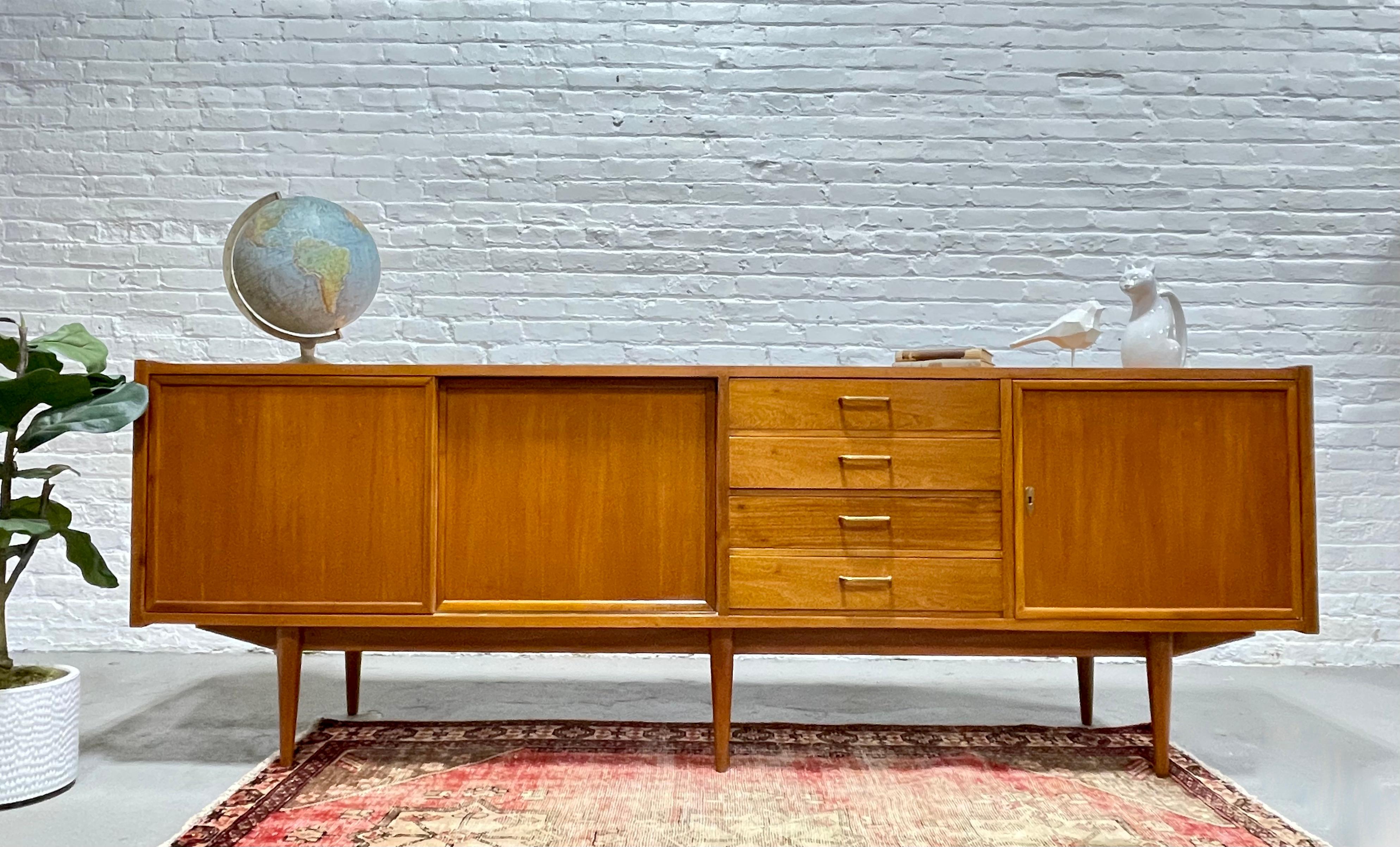 EXTRA LONG and just plain “EXTRA” in every sense. This Mid Century Modern Italian credenza, c. 1955, is an absolute showstopper, boasting simple yet classic styling with brass hand pulls, long tapered legs and lovely butterscotch coloring. Along