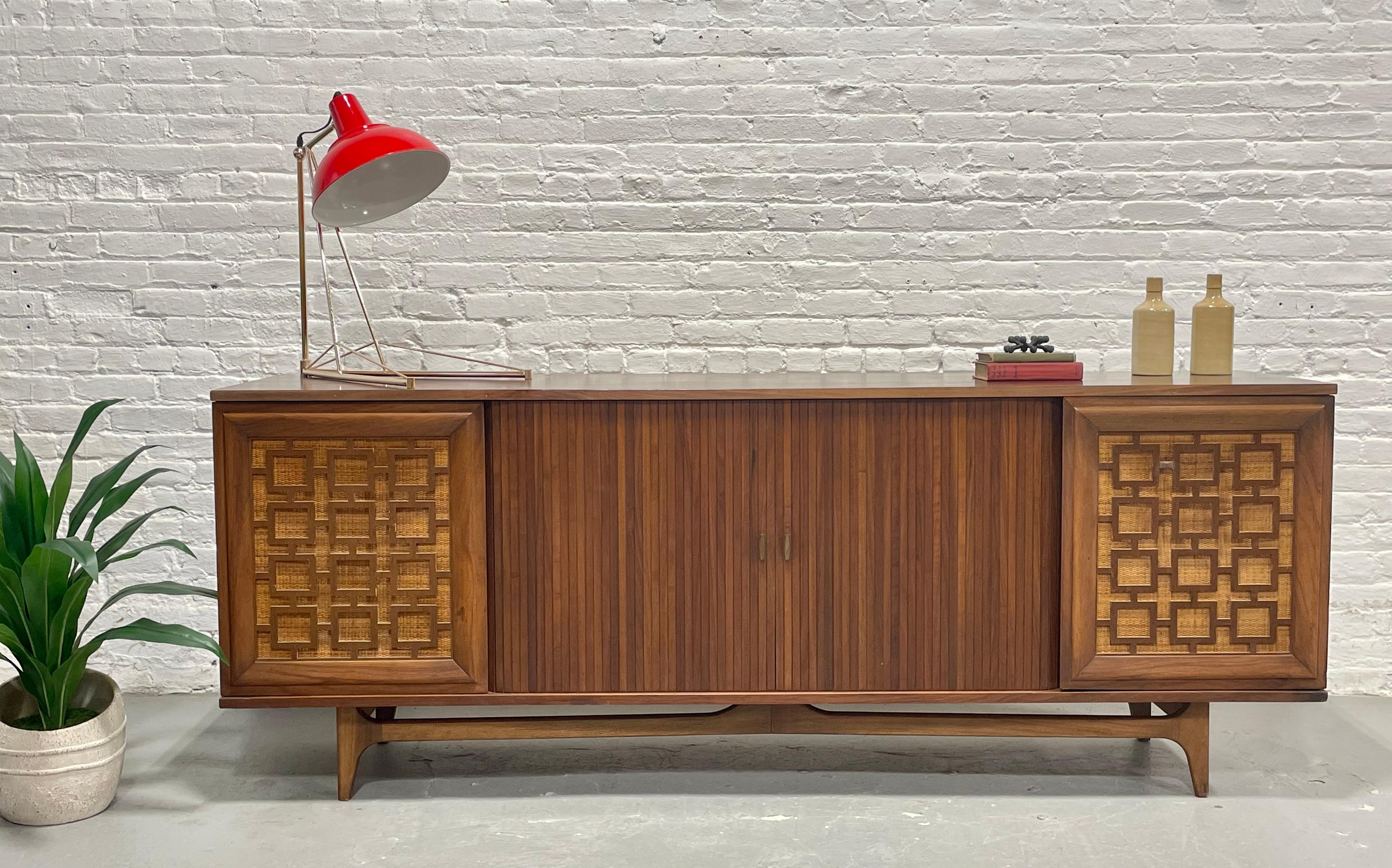 An exceptional Mid Century Modern walnut credenza showcasing refined craftsmanship and playful design. The center section is fitted with sleek tambour doors that smoothly glide open to reveal an expansive interior storage space. Flanking side