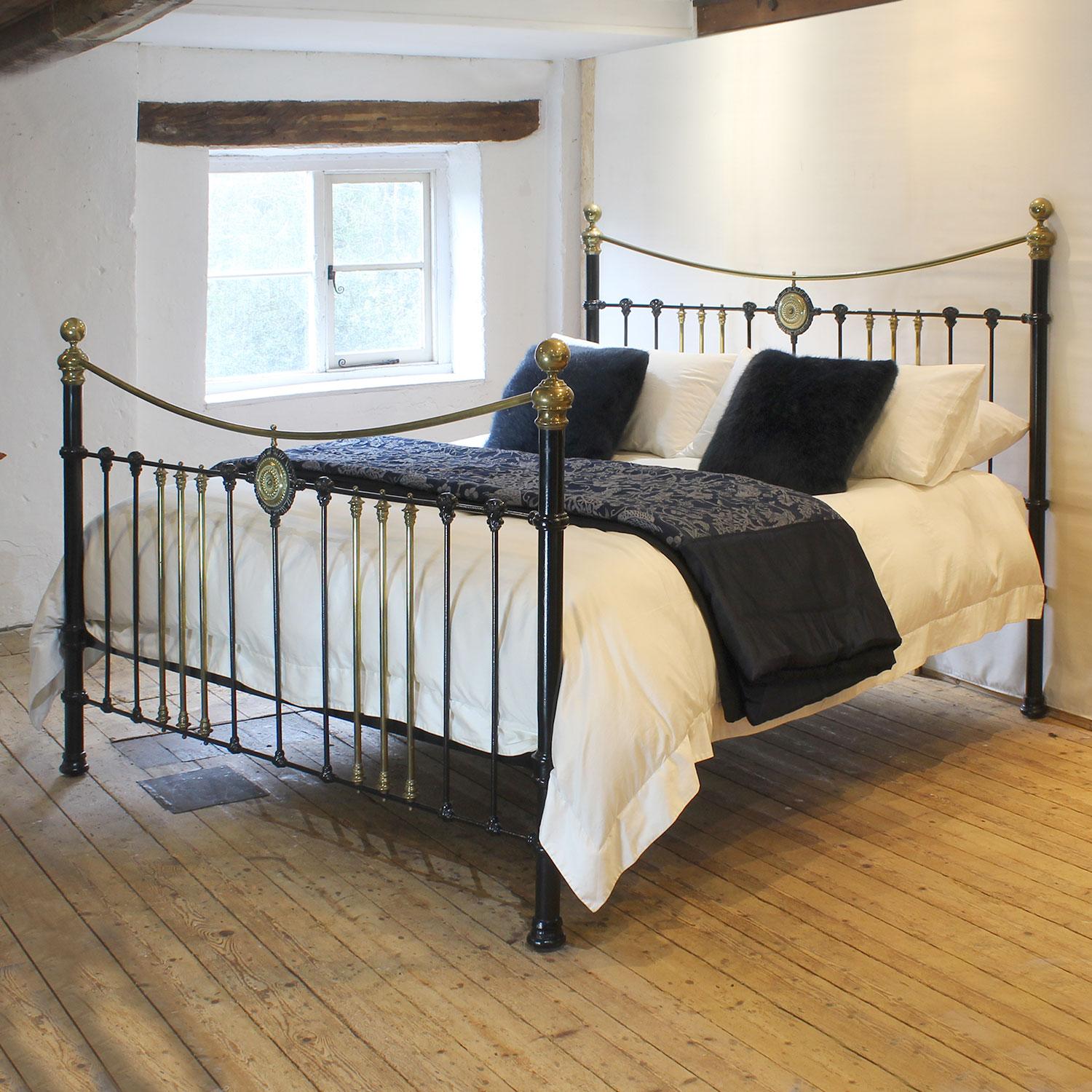 An attractive 6ft wide (72 inches) brass and iron bedstead finished in black with central brass rosette decoration and curved brass top rail, adapted and extended from an original Victorian frame, circa 1895. The brass work has acquired a tarnished