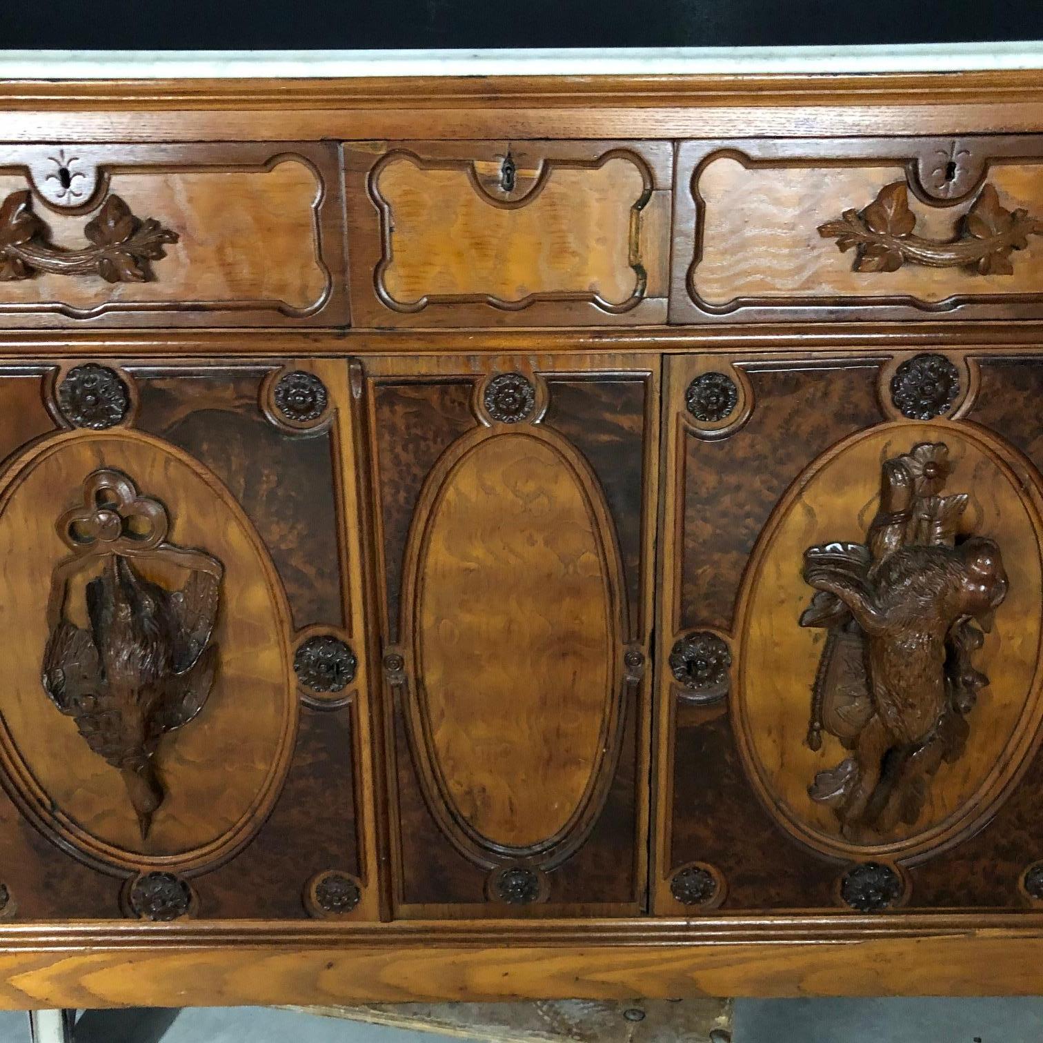 Handsome exquisitely carved hunt cabinet with 3 dimensional hare and fowl. The cabinet is gracefully curved on the corners with two doors which exhibit a Black Forest type carving. Three drawers open below the Carrara marble top. It has a walnut