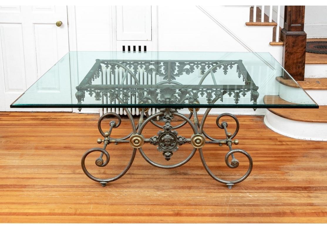 A Classic French pastry table base in iron with brass accents with particularly elaborate metal-work topped with a thick glass top suitable for dining, work or center table. With a scalloped scrolled frieze with pendant buds. The centers with