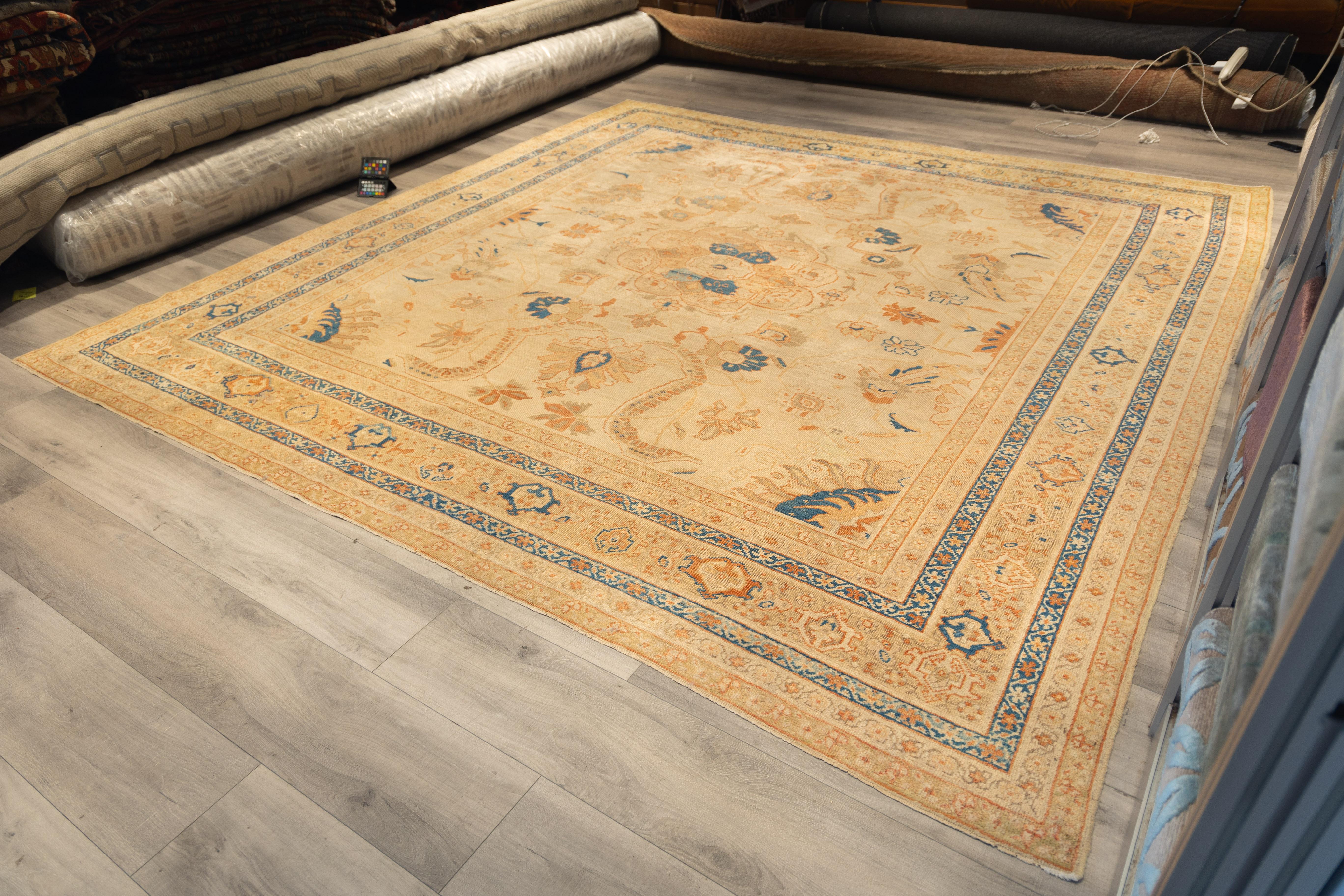 La extraordinaria alfombra antigua Sultanabad Rugs presenta un diseño amplio y simétrico centrado en torno a un audaz medallón formado por suaves elementos florales coralinos y azul marino. El campo está pintado con un fondo marfil apagado, adornado