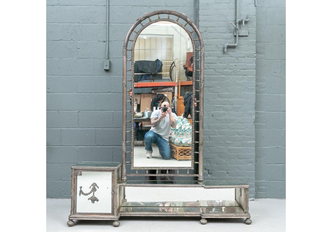 A fine art deco mirrored and silver-plated bronze vanity with neoclassical design elements. Comprised of an arched and reeded mirror with mirrored base with storage. The mirror with a relief banding of flowers and an openwork reeded gallery with