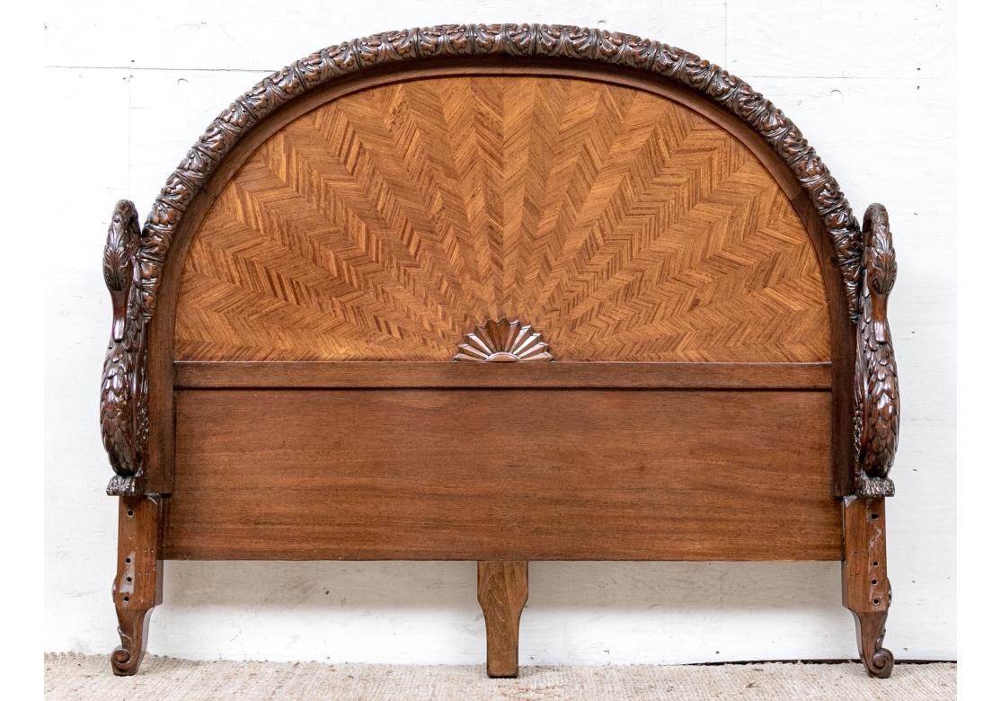 An elaborately carved full bedstead with intricate swan carvings. The headboard with a gadrooned carved acanthus motif trim around the parquetry herringbone inlay. The arched headboard is flanked by two heavily carved long necked swans. A third swan