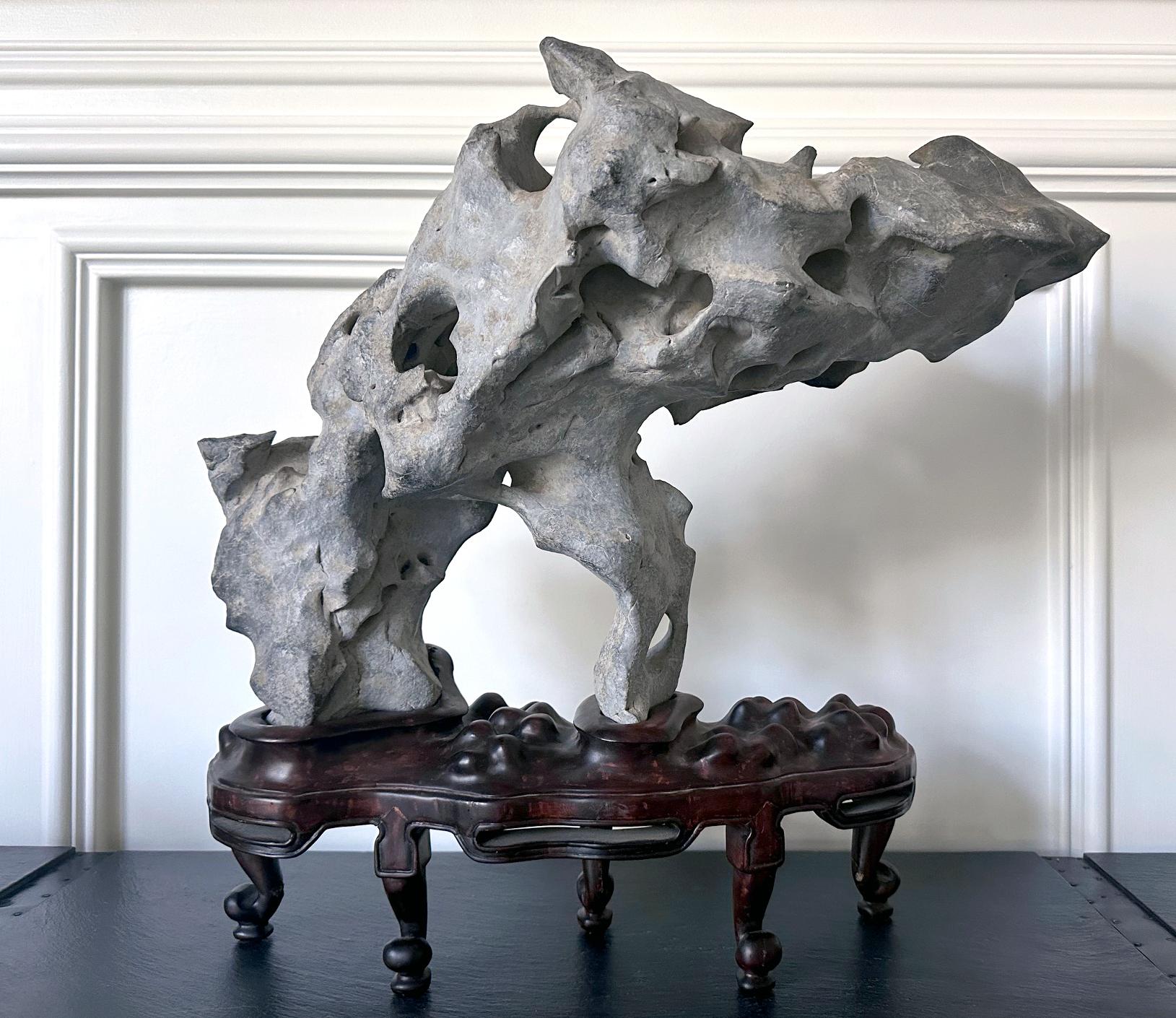 A stunning Taihu scholar stone in an unusual horizonal balanced form perched on a custom wood stand. The stone, in a nearly pure greyish white color, display a weathered smooth surface with visually arresting natural geological characters. The