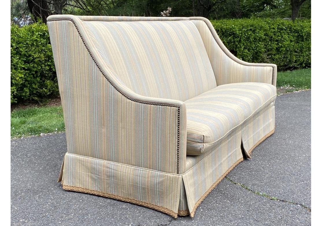 A fine and Classic Style sofa from Tomlinson with notable Custom Tailored Upholstery. The square frame with short wings into deep sloping arms. Upholstered in a pale stripe in tan, green and gold tones, with nail head trim along the back and sides.