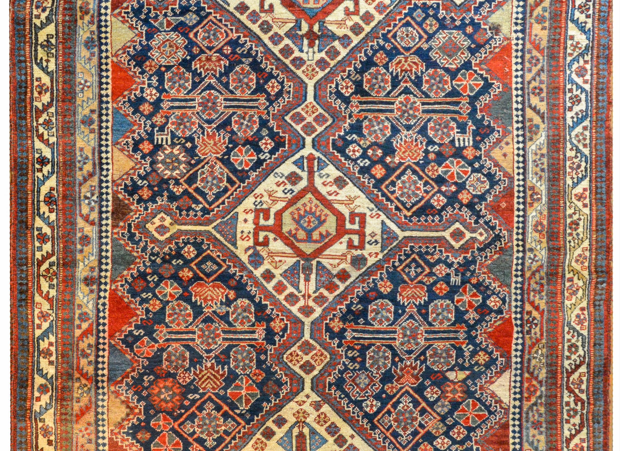 An extraordinary early 20th century Persian Ghashgaei rug with three large central diamond medallions on a field of densely woven myriad stylized flowers and goats woven in crimson, light indigo, and cream, on a dark indigo background. The border is