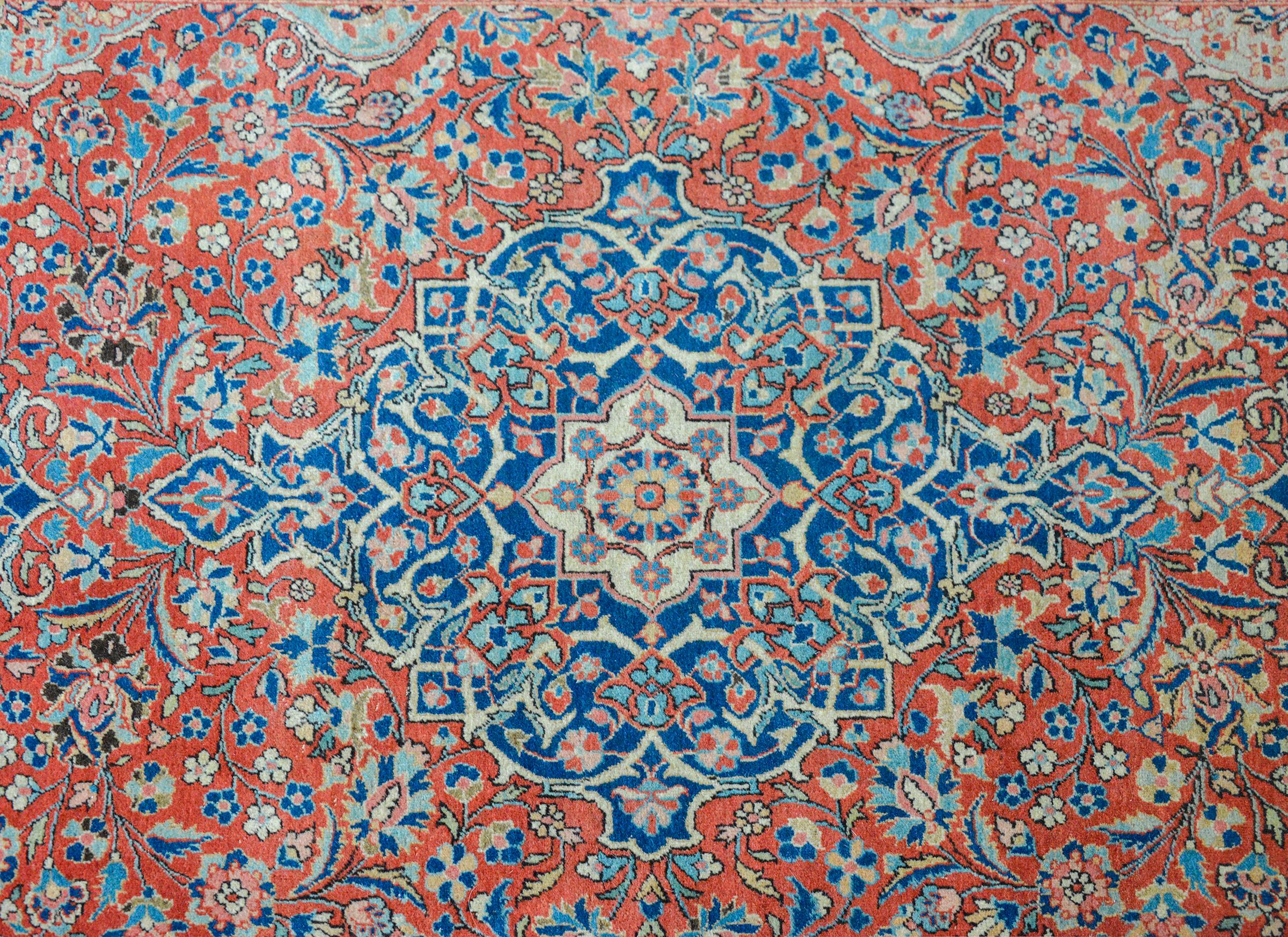 An extraordinary early 20th century Persian Kashan rug with an intricately woven pattern with a central medallion living amidst a field of scrolling vines and flowers, all woven in light and dark indigo, pink, gold, and cream against a crimson