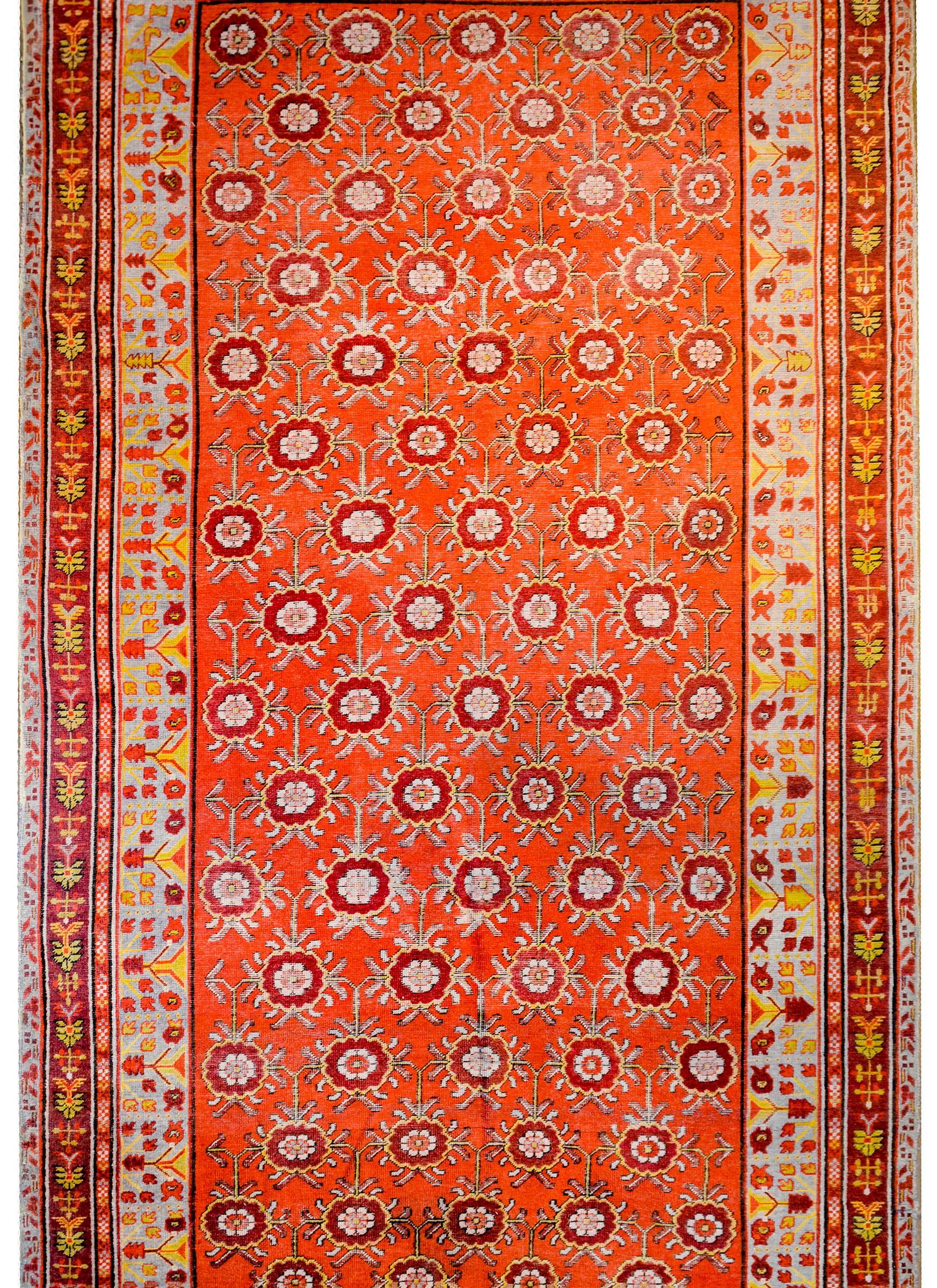 An extraordinary early 20th century Central Asian Samarghand rug with an incredible all-over large scale trellis peony pattern woven in dark cranberry and gold on a brilliant coral colored ground. The border is complex with multiple floral patterned