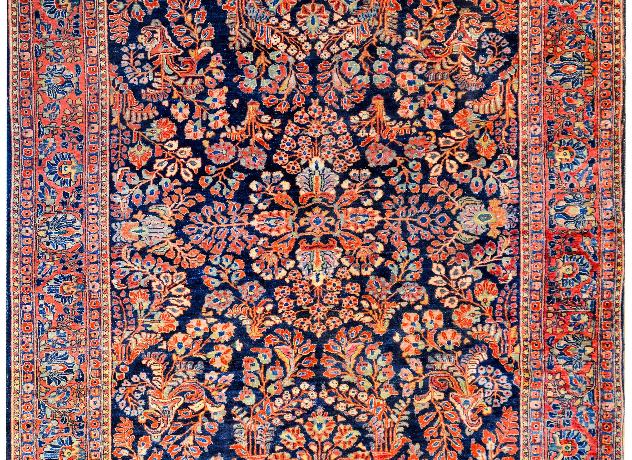 A wonderful early 20th century Persian Sarouk rug with a beautiful all-over mirrored floral pattern woven in crimson, pink, cream, and light indigo on a dark indigo background. The border is typical with a wide band with large-scale floral and vine