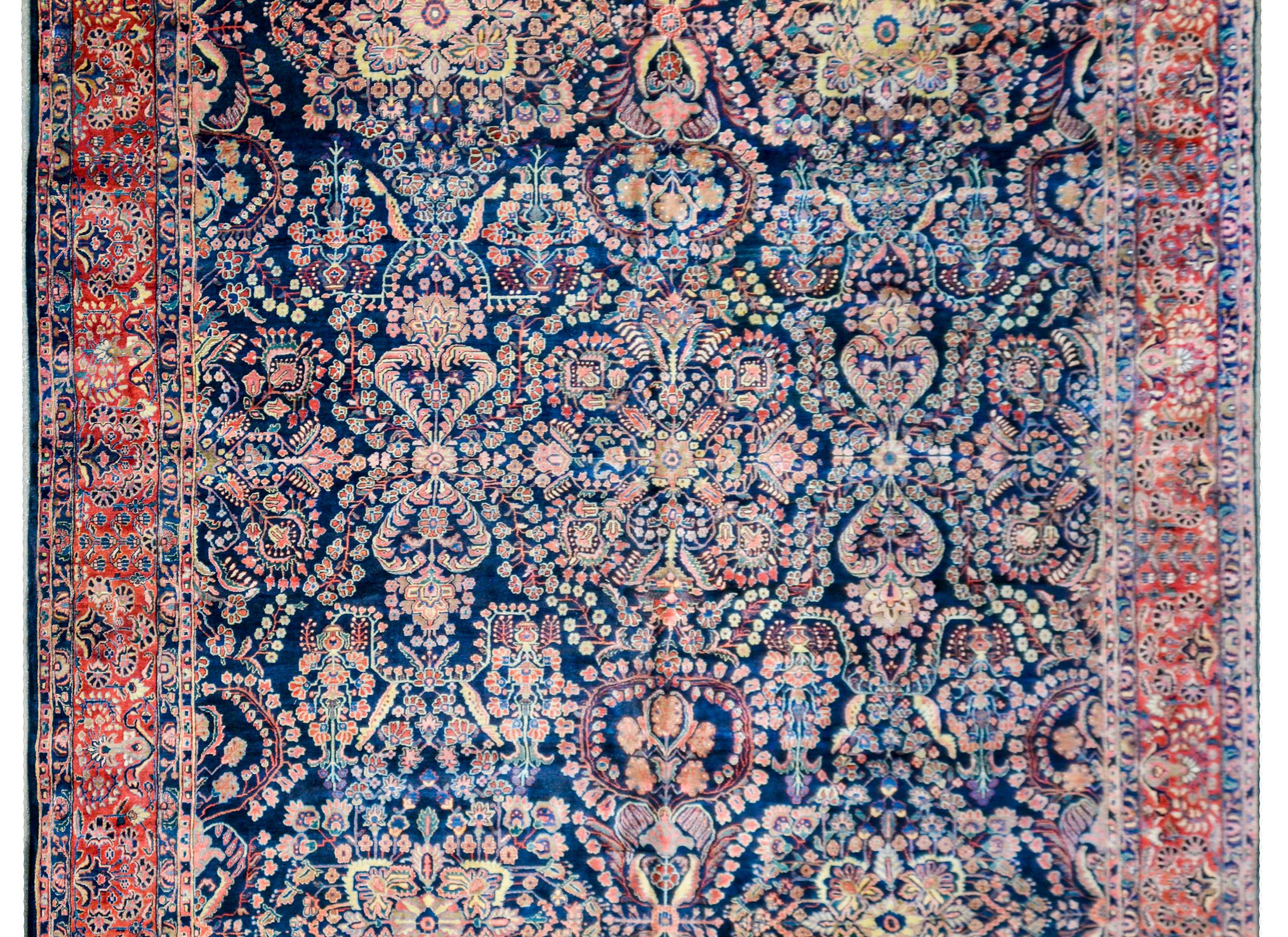 This is one of the most extraordinary early 20th century Persian Sarouk rugs we've ever seen! The central field is composed with large-scale mirrored floral pattern woven in crimson, pink, light and dark indigo, on a bold dark background. The border