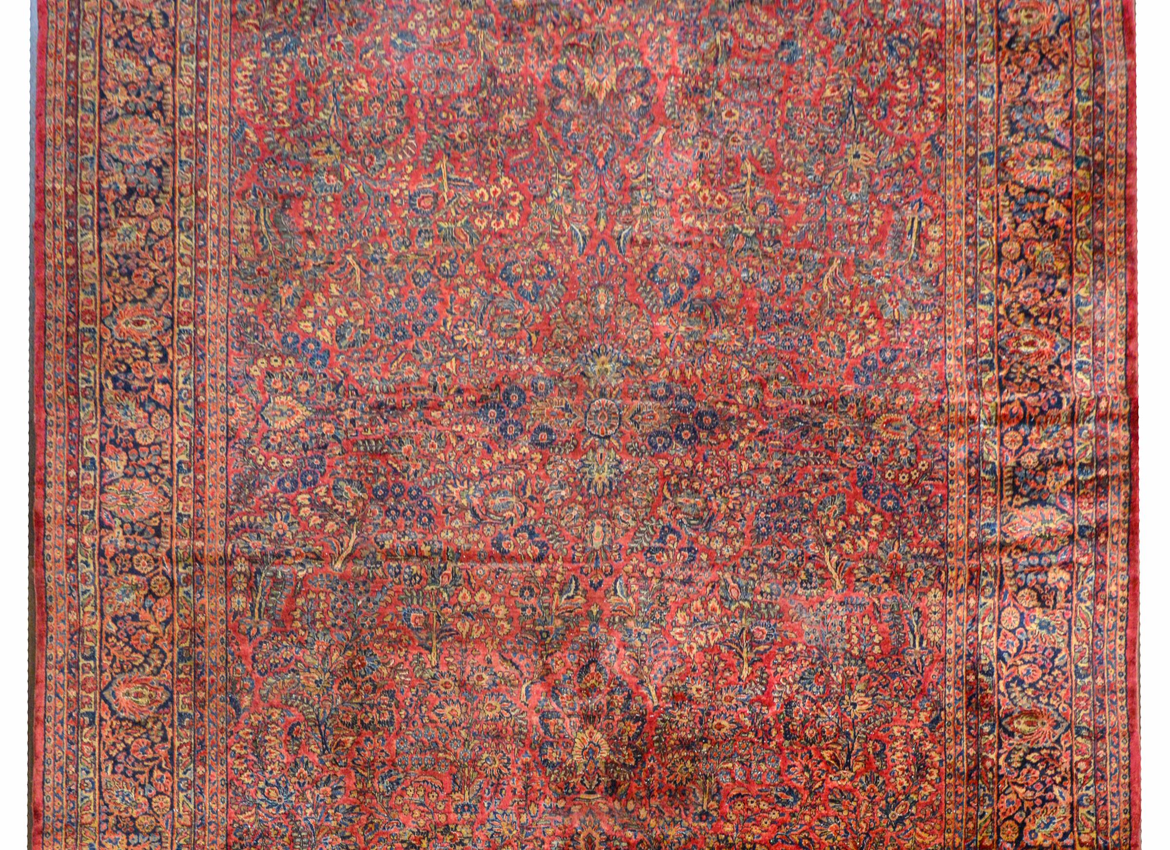 An extraordinary early 20th century Sarouk rug with an elaborate all-over pattern containing myriad flowers woven in traditional Sarouk colors of light and dark indigo, cream, pink, and crimson, all on a cranberry background. The border is elaborate