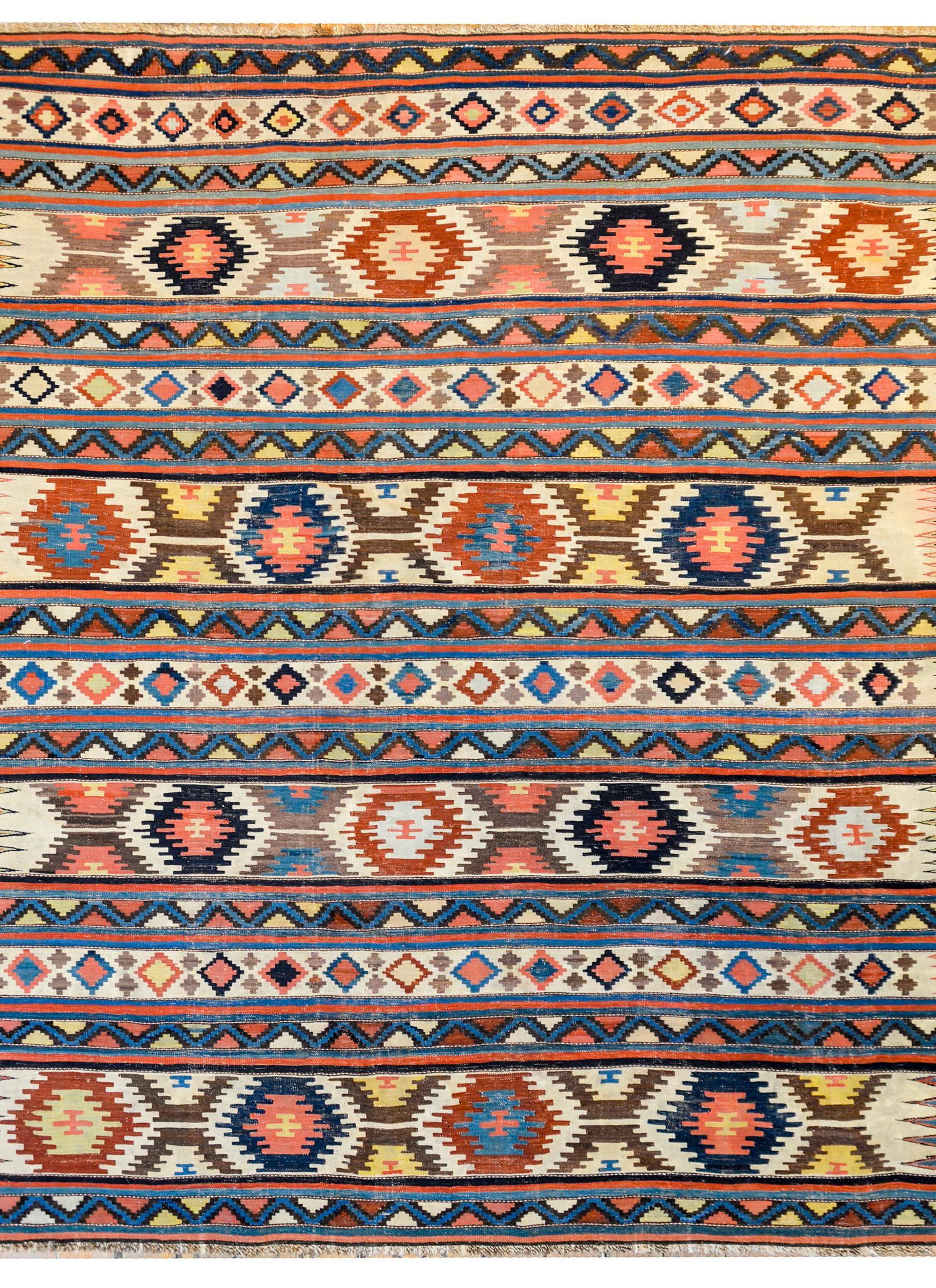 An extraordinary early 20th century Persian Shirvan kilim rug with myriad multicolored and geometric patterned stripes woven in indigo, crimson, gold, cream, coral, and brown vegetable dyed wool.