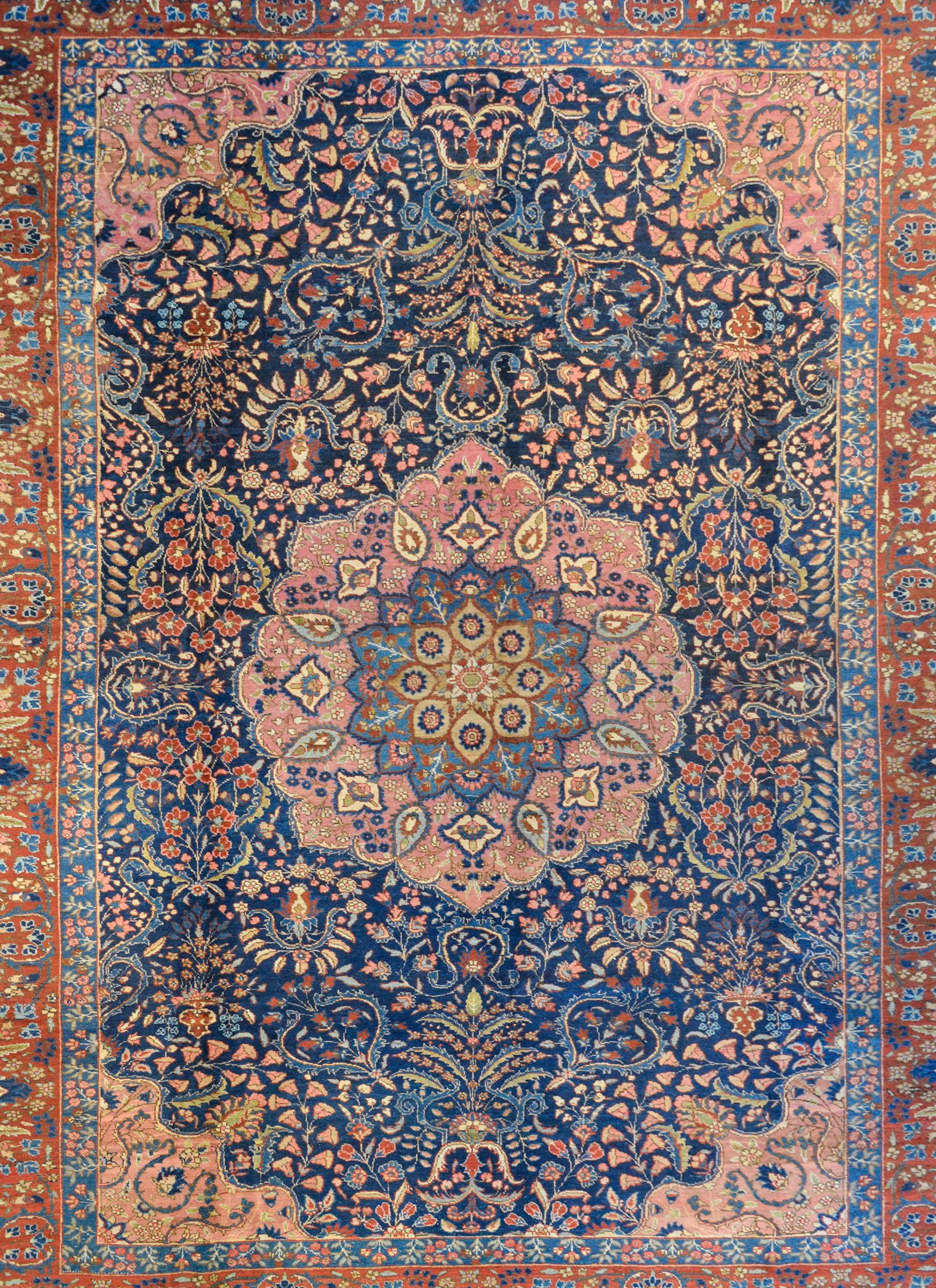 An extraordinary early 20th century Persian Tabriz rug with a beautiful large round floral medallion woven with a petite floral and scrolling vine pattern rendered in crimson, gold, light and dark indigo, green, and pink. The medallion lives on a