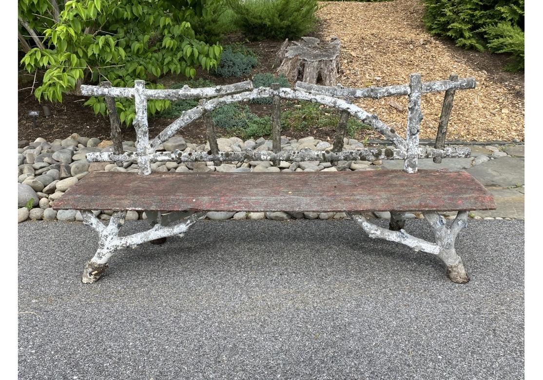 Remarkable cast cement Faux Bois bench with classic Openwork form in all original and authentic condition, likely French. The tree branch back in old white paint, and a seat in old red paint with sloping front edge. . Raised on splayed tree branch