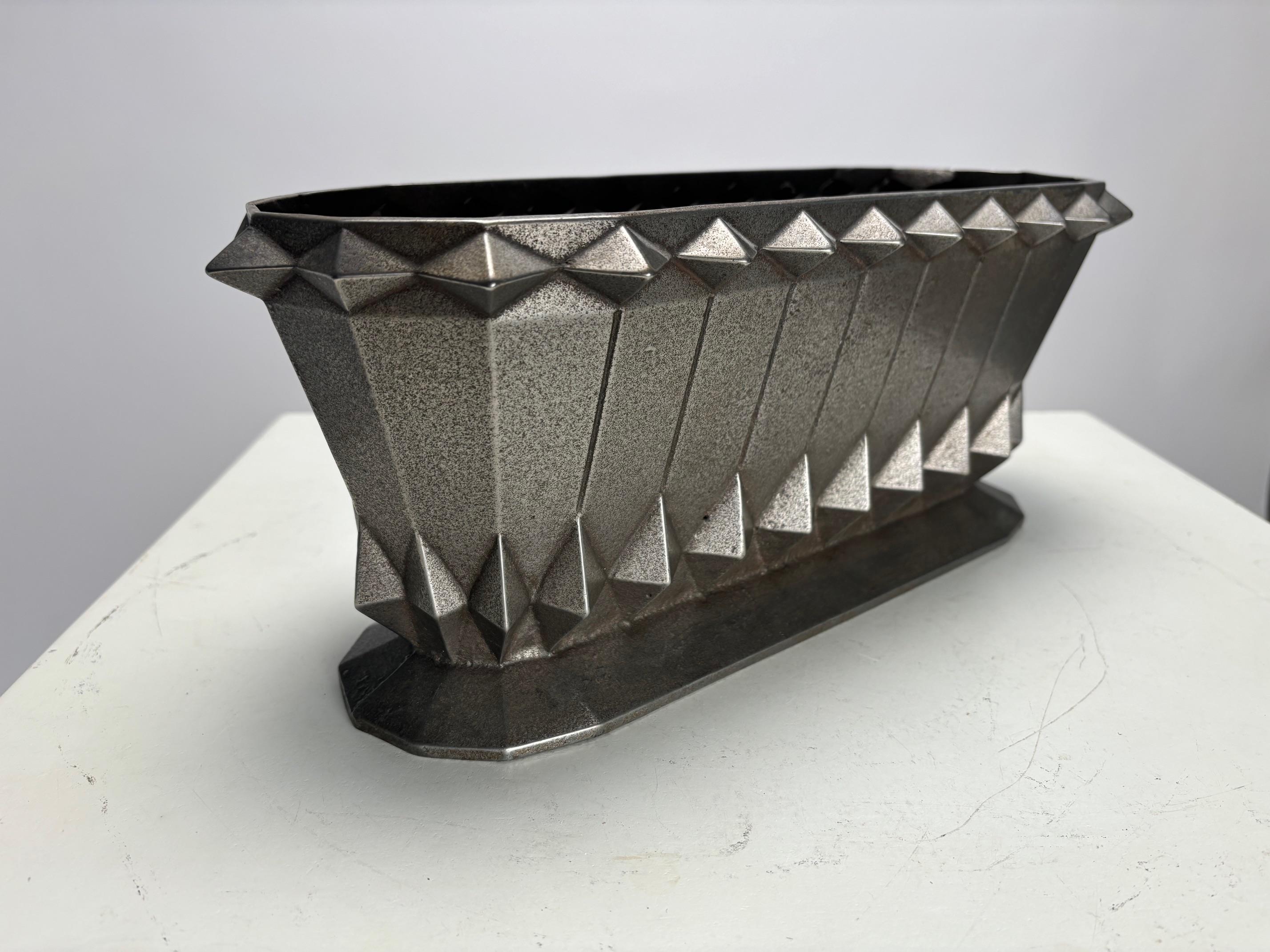Questo raffinato vaso in ghisa, ispirato all'Art Déco francese, evoca magistralmente lo spirito iconico del Chrysler Building di New York, il capolavoro architettonico di William Van Alen del 1930 che incarna l'audace eleganza e la dinamica