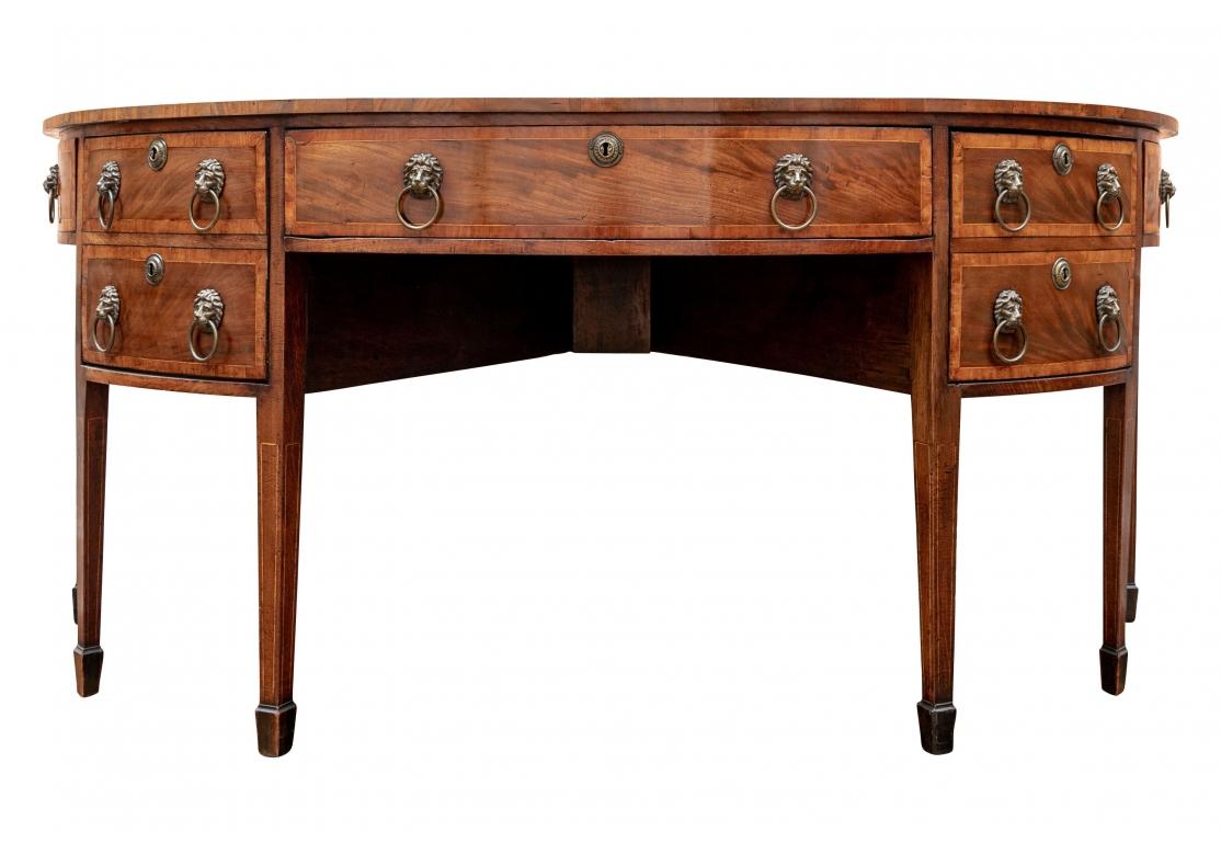 George III mahogany demilune inlaid sideboard with satinwood banding, two cellarette drawers on tapered legs with spade feet. English, circa 1780 - 90. The sideboard with inlaid shell motifs with string inlay and radiating to a scalloped motif. The