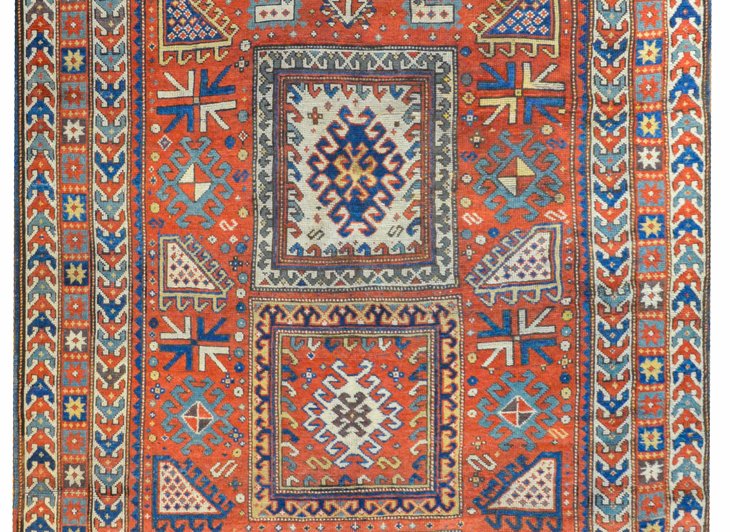 An extraordinary late 19th century Persian Kazak rug with an outstanding tribal pattern containing myriad geometric stylized flowers woven in indigo, gold, green, cream, and white, on a rich crimson background, surrounded by multiple narrow