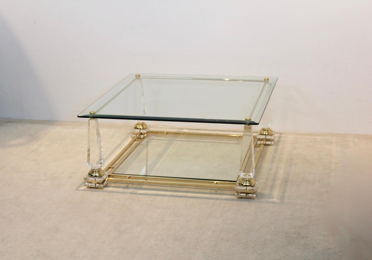 Sophisticated Dutch coffee table with brass frame, with glass plates and with Obelisk shaped Lucite legs. This light and glossy square table with beautiful brass accents has two-tier glass. The table is a unique example of the Hollywood Regency