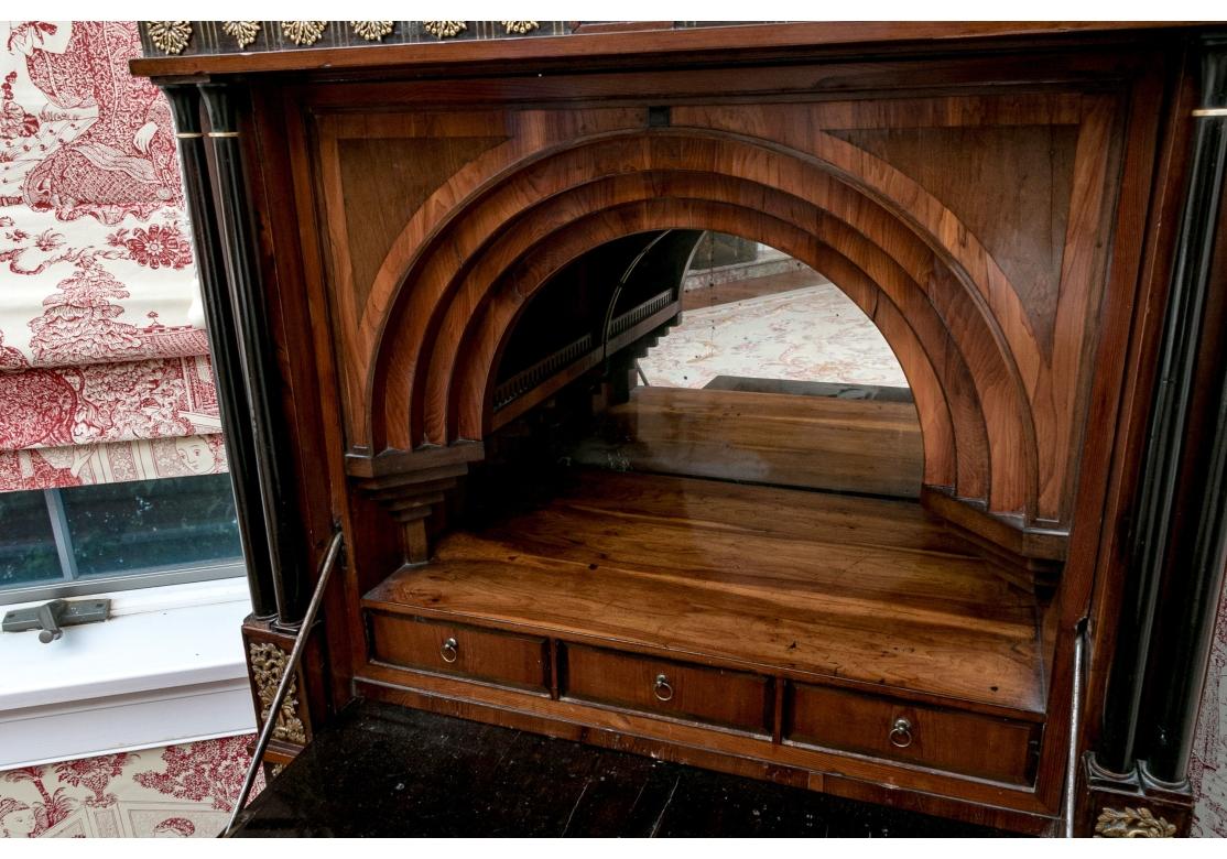 Secrétaire à abattant avec un capuchon arqué et une façade tombante décorée de façon élaborée avec des incrustations de laiton et de cuivre, ainsi qu'une tirette en forme de scarabée. La porte cintrée s'abaisse pour révéler un espace de rangement
