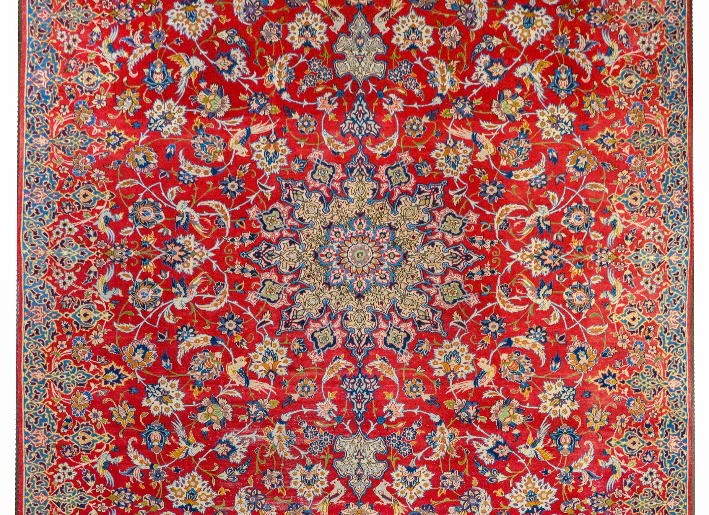 An extraordinary mid-20th century Persian Isfahan rug with an outstanding large-scale medallion amidst a field on of scrolling vines and flowers woven in myriad colors on a brilliant crimson background. The scrolling vines of the field morph into