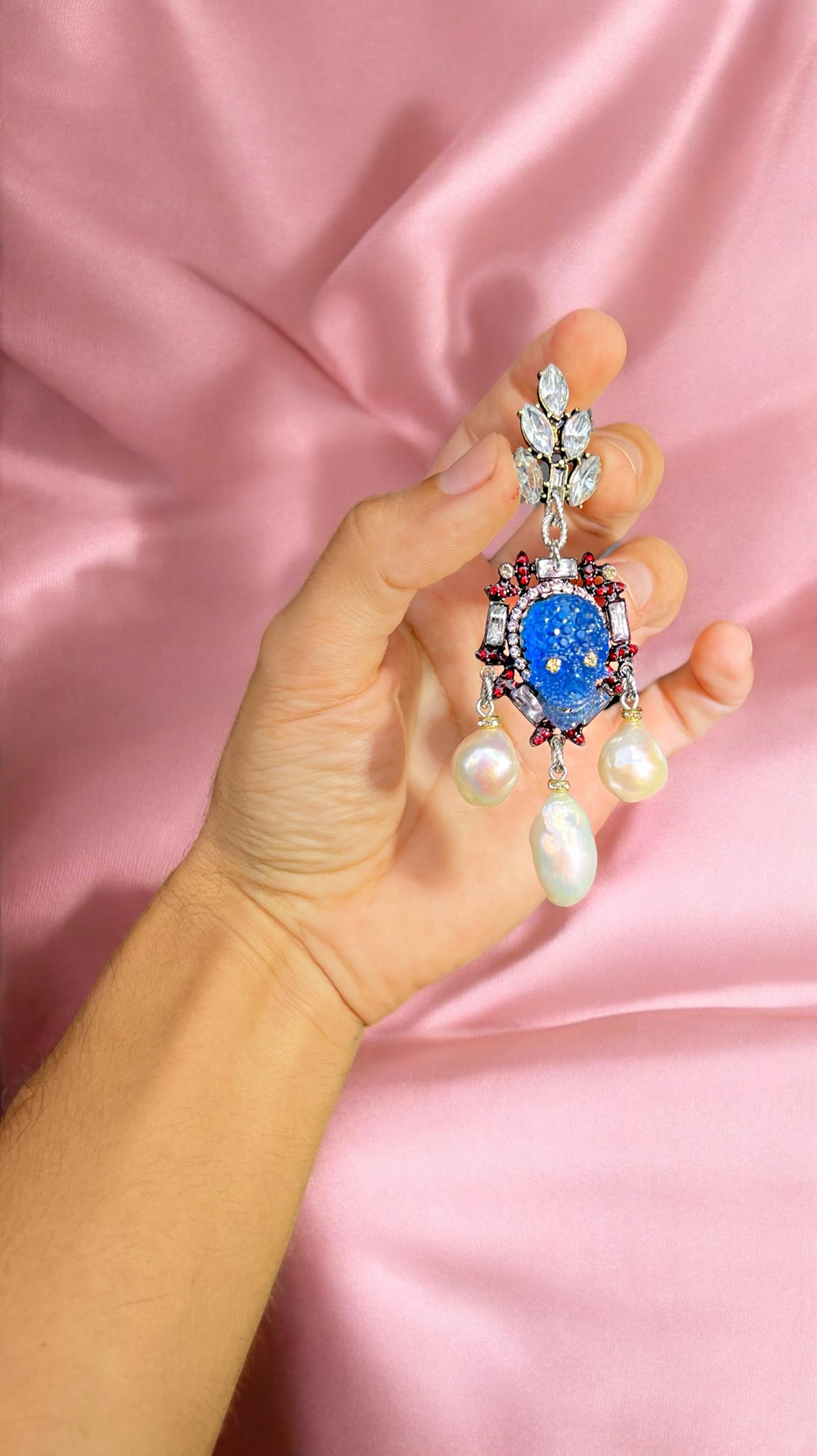 These unique, one-of-a-kind pair of earrings is truly a statement of artistry, never to be repeated. Featuring a delicate cluster of crystals, they catch the light from every angle. Dangling below is a crystal-encrusted frame adorned with rich red
