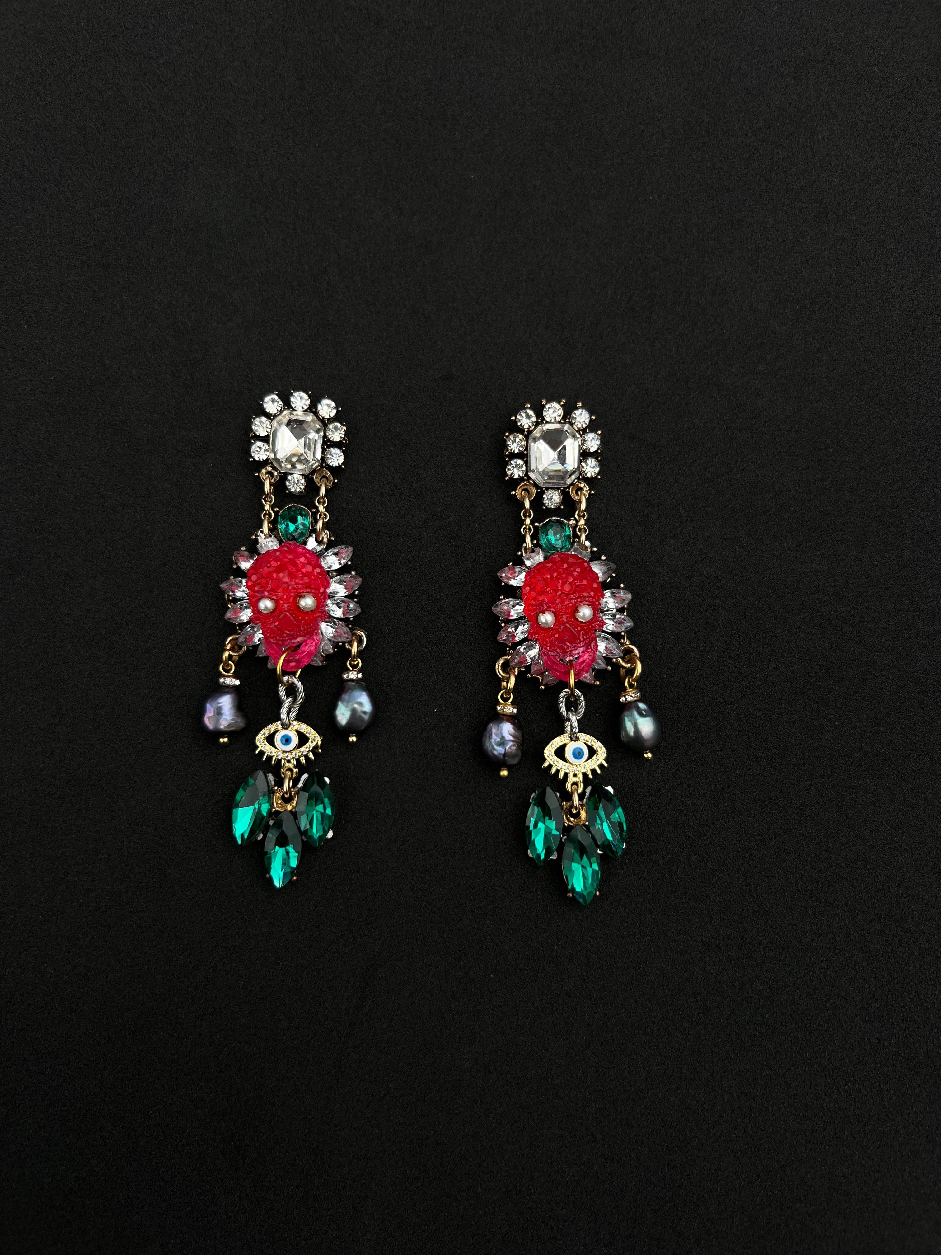 These one-of-a-kind, handmade chandelier earrings are crafted to perfection, with only one pair in existence that will never be repeated. At the center of each earring is a striking fuchsia skull, adorned with pearl-embedded eyes, creating an