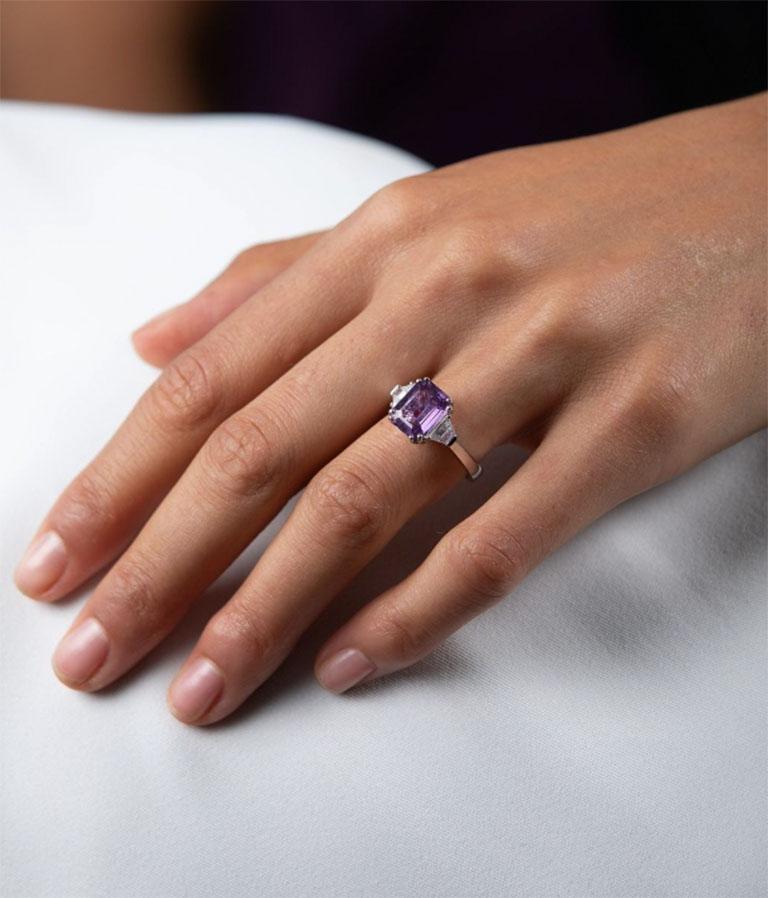 Playful yet sophisticated, this three-stone ring features a deep purple sapphire as its commanding centre stone. Cut in a lively octagon shape, the sapphire is comfortably positioned between two white trapeze diamonds and showcased on a simple white
