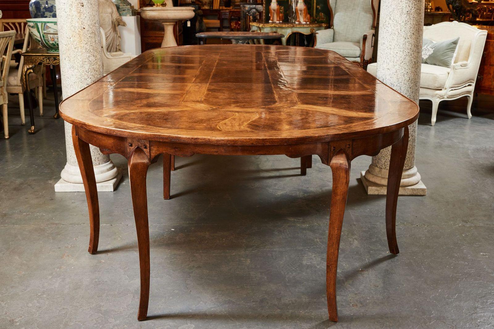 An enormous, vintage, walnut and pecan wood, inlaid dining table with a total of six, extension leaves. The top featuring a striking pattern of wave-like, radiant tendrils along a central axis. The table is nine feet on its own, but with the