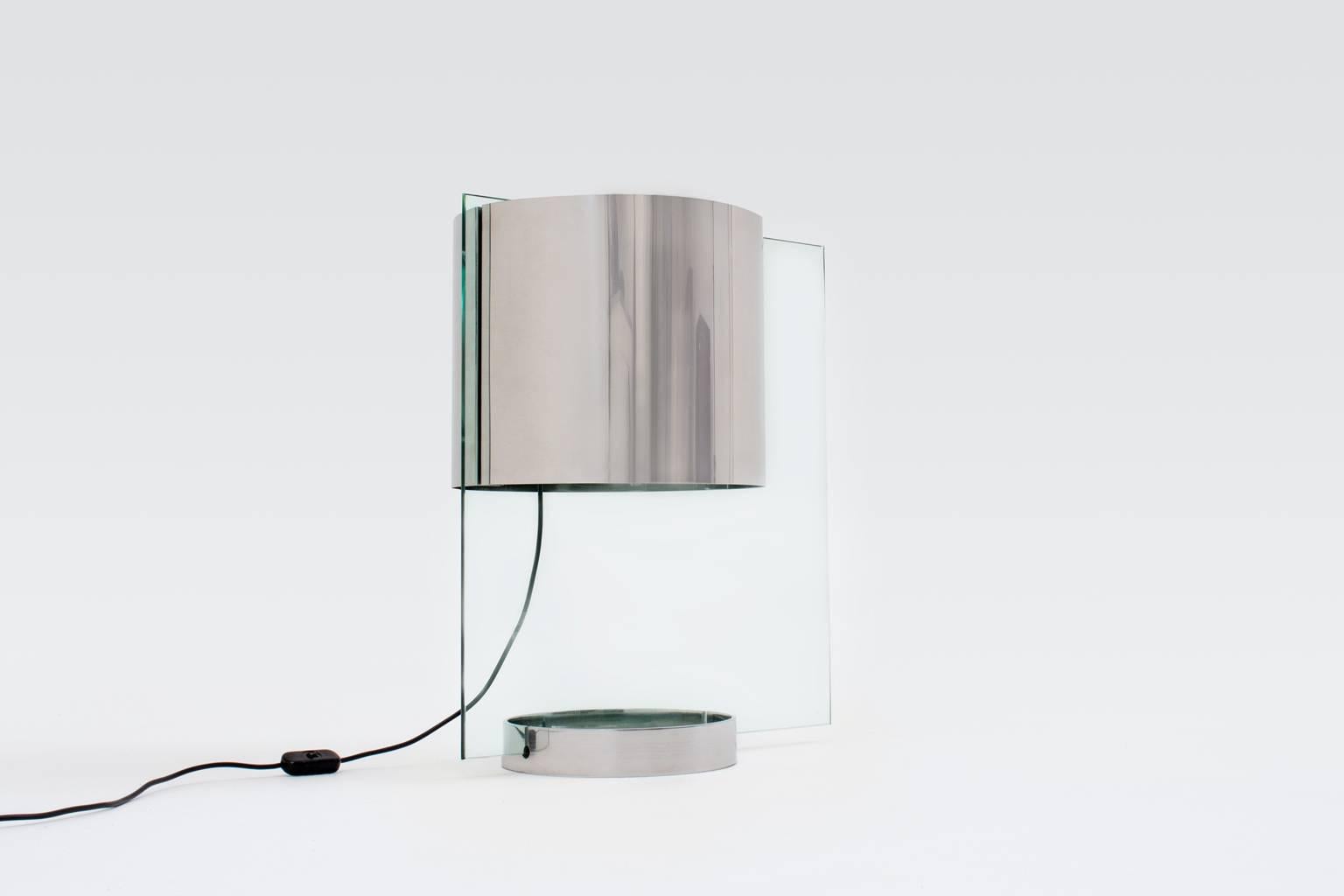 Rare table lamp by Lumenform, Italy, 1970. Extraordinary design made from a rectangular sheet of glass and stainless steel shade, base and lighting part.
This sophisticated sharp lined lamp provides a very nice light, light is transported true the