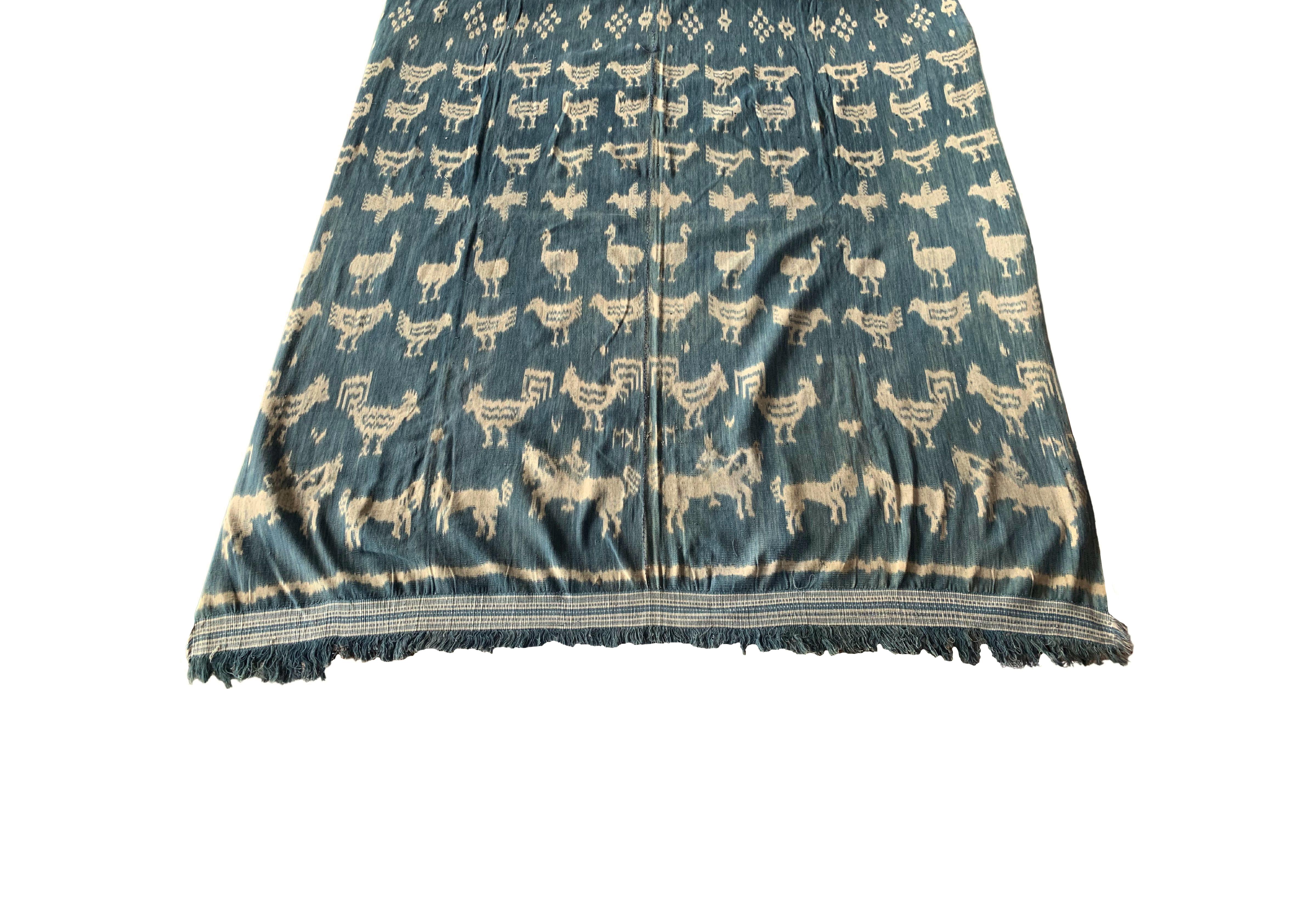 This Ikat textile originates from the Island of Sumba, Indonesia. It is hand-woven using naturally dyed yarns via a method passed on through generations. It features a predominantly indigo blue background with chicken motifs and distinct tribal