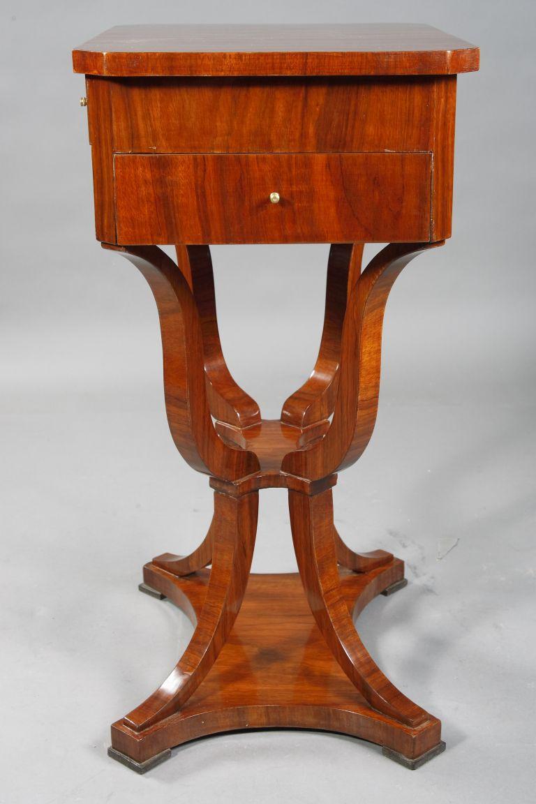 Mahogany on solid beechwood. On strongly curved, cornered legs connected by an easily intervening intermediate compartment and then go off saber-shaped legs on four sided retracted, base plate on disc feet off. Two-drawer frame base, upper drawer