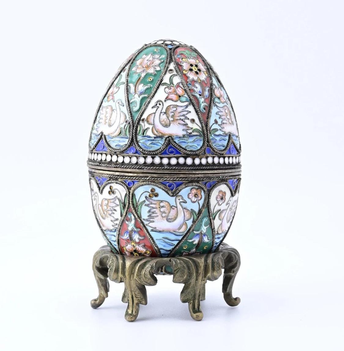 This Ornate Decorative Egg is a stunning piece. Featuring intricate enamel work with swan and floral motifs, it captivates with its vibrant colors and detailed artistry. The egg's design is meticulously crafted, with each panel showcasing a unique