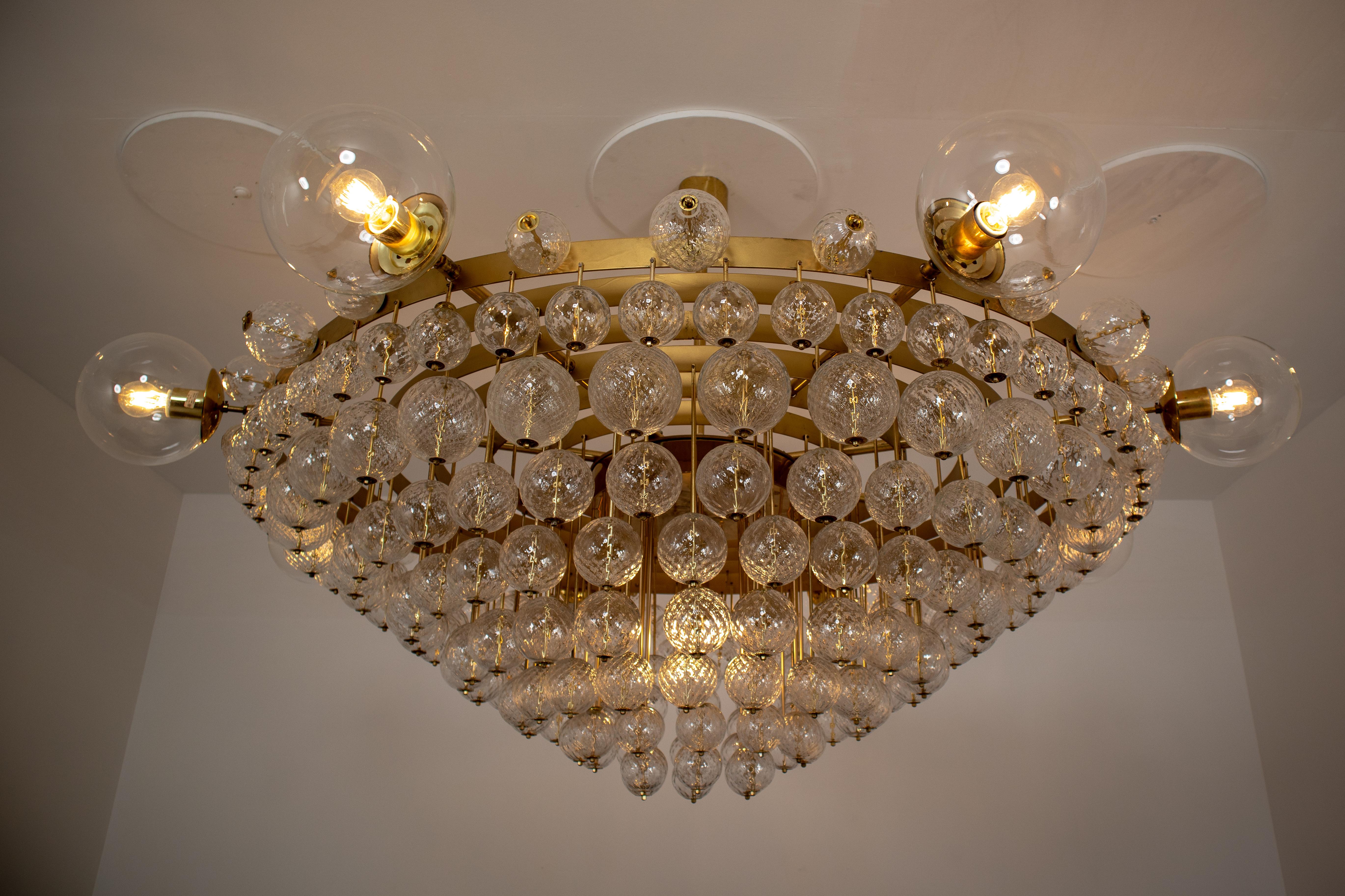 Extremely large 7.5 ft midcentury hotel chandelier with brass fixture, 8 large hand blowed glass globes and innumerous smaller structured glass globes. The chandelier with brass frame consist of 9 lights, formed in a circle. The pleasant light it