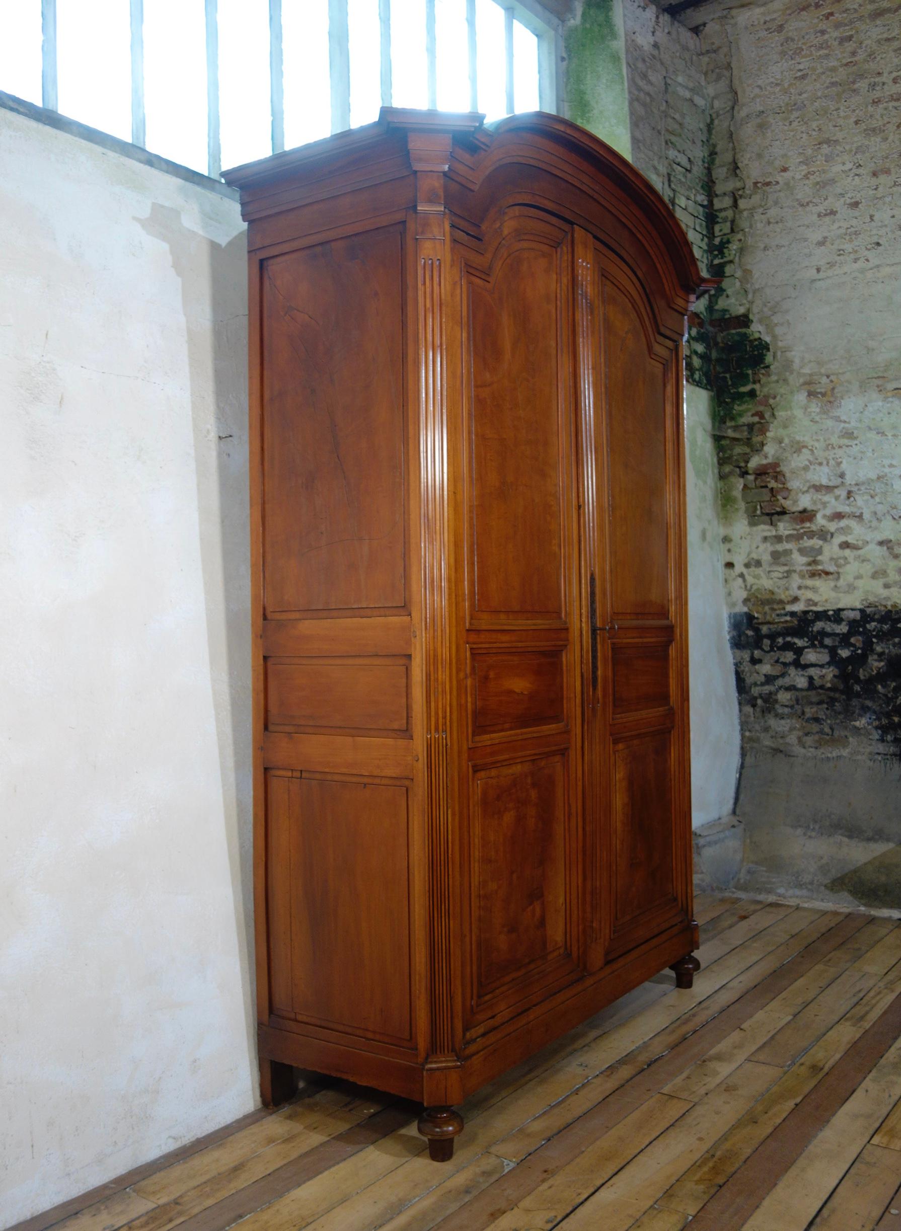 An extremely large Louis XVI walnut armoire, displaying a domed and molded cornice with projecting canted corners. This armoire demonstrates simple inset triple paneled doors, separated by a relief reeded pilaster. Each of the doors features