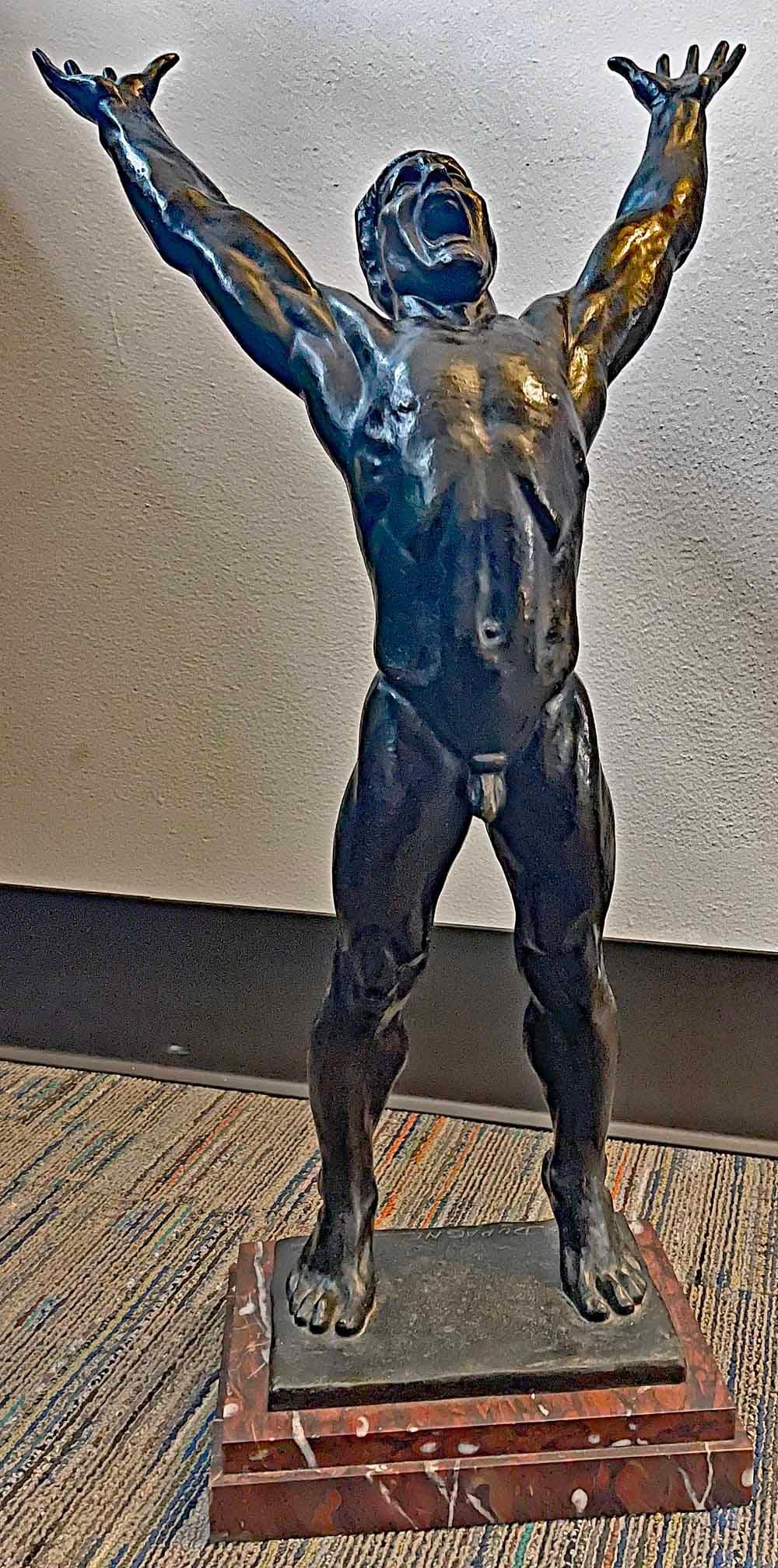 Extraordinariamente poderosa y muy rara, esta gran escultura de bronce de una figura masculina desnuda, obra de Arthur Dupagne, le muestra estirándose y haciendo fuerza hacia arriba, con la cabeza echada hacia atrás y gritando de exultación.  Fue