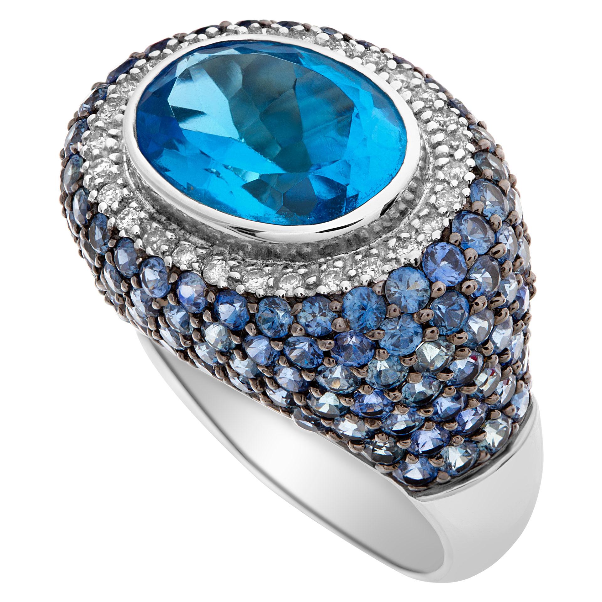 Eye catching cocktail ring with a 7 carat oval cut blue topaz surrounded by blue sapphires & diamonds set in 14K yellow gold. 28 round cut diamonds approximately total weight 0.23 carat and 152 round cut blue sapphires approximate weight 6