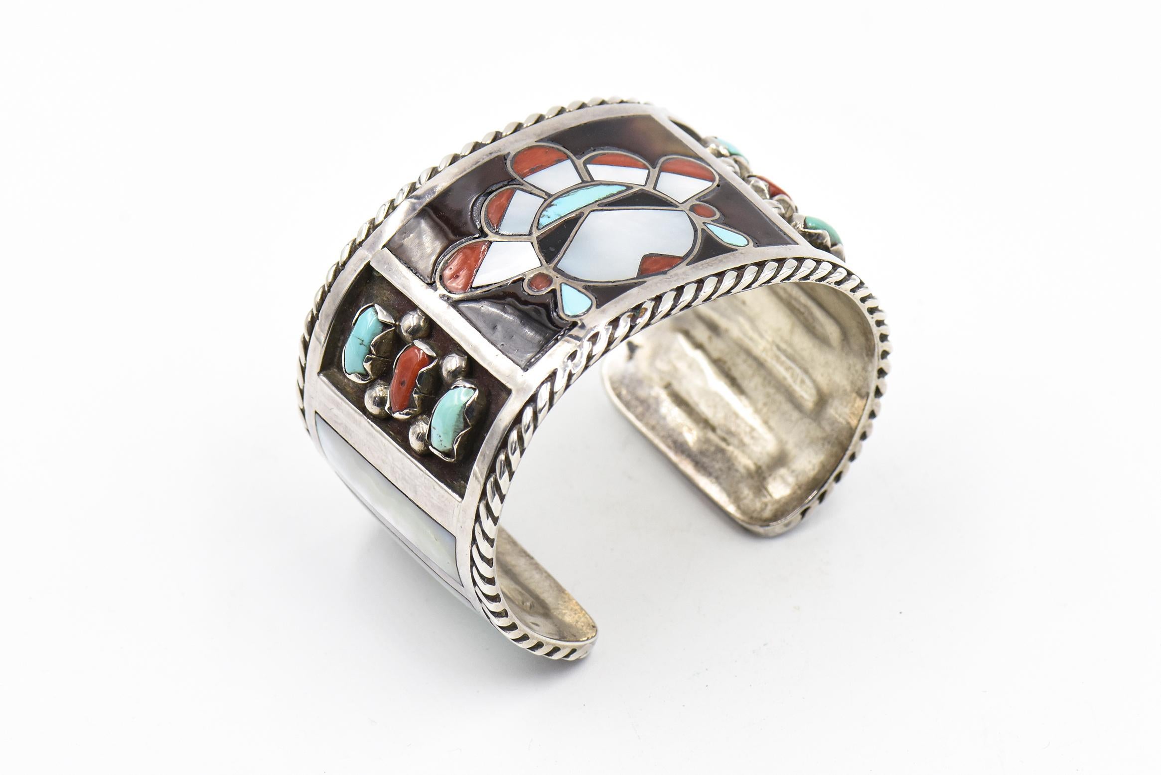 This beautiful bracelet is by Zuni artists Filbert & Clara Gasper.  Circa 1960 - 1970.  The bracelet is sterling silver with inlay turquoise, mother of pearl and coral.  In the center is an inlaid face and on the sides there are additional bezel set