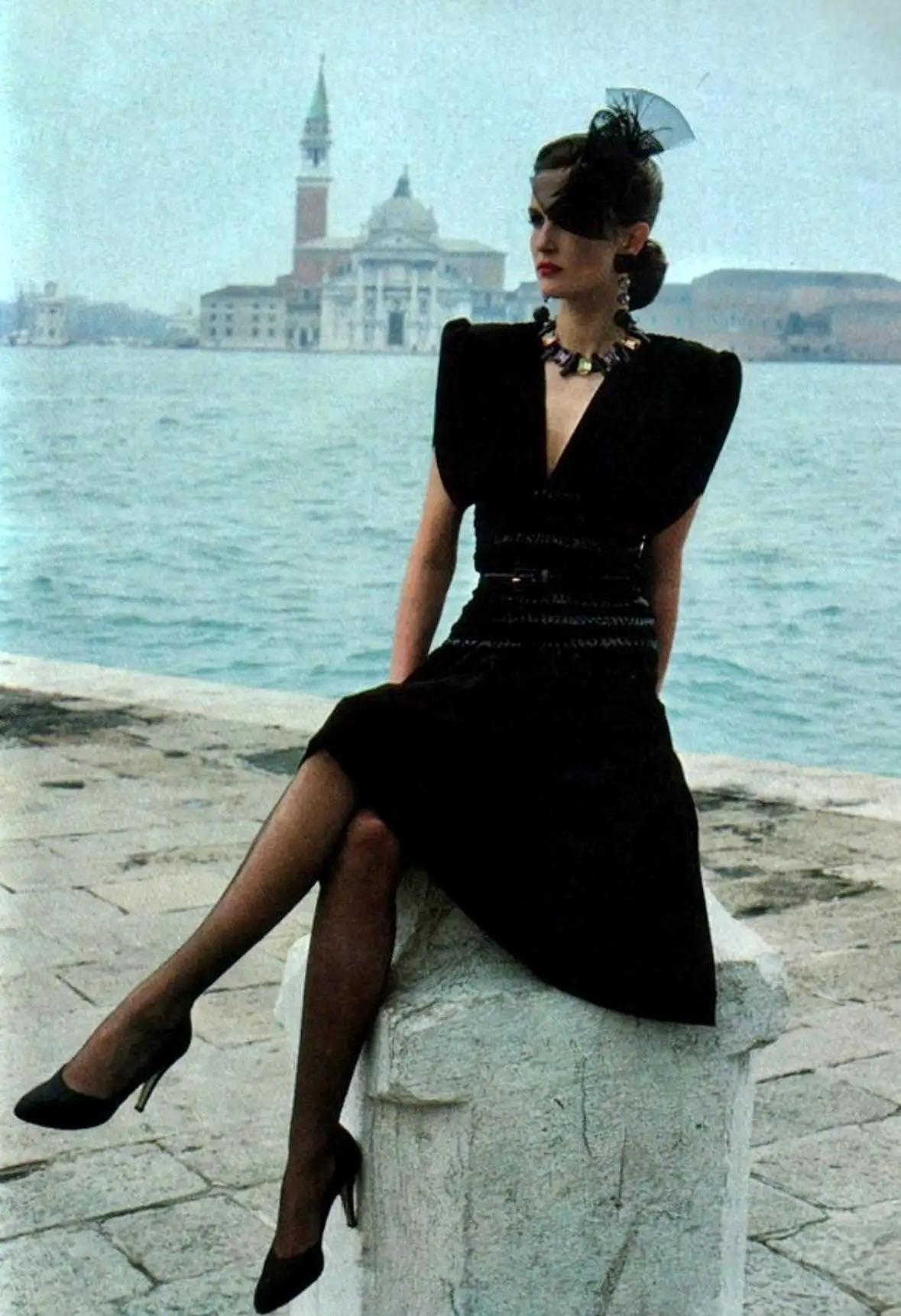 Issue de la collection Automne/Hiver 1983, cette fabuleuse robe noire ruchée Saint Laurent Rive Gauche, créée par Yves Saint Laurent, a été mise en valeur dans la campagne publicitaire de la saison, photographiée par Helmut Newton à Venise. Des pad