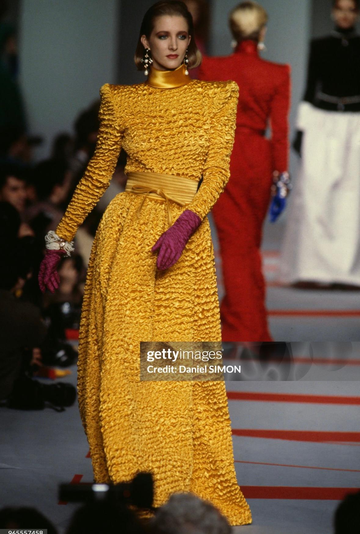 From the Fall/Winter 1986 collection, this ruched black satin Valentino Garavani skirt set is comprised of a short-sleeve blouse and a matching full-length skirt. The season featured similarly designed ruched pieces, with the long-sleeve yellow