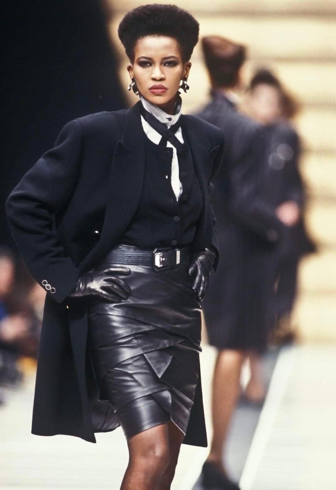This Fall/Winter 1987 Gianni Versace runway black leather ribbon-tiered pencil skirt showcases leather layering, creating a striking tiered effect. Worn on the runway by Amalia Vairelli, it embodies the dramatic elegance and craftsmanship that