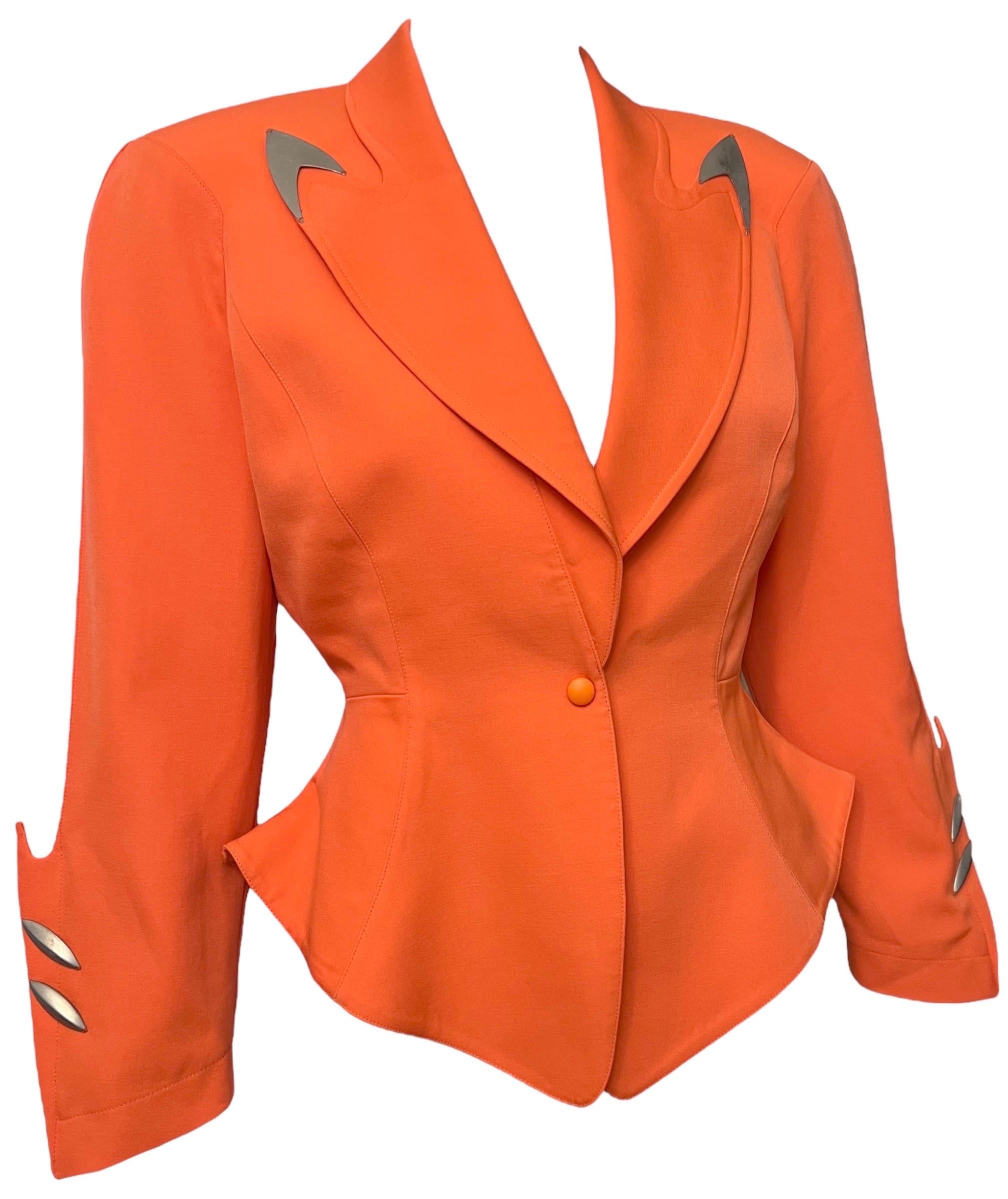 Thierry Mugler futuristic vivid orange jacket from the Fall Winter 1989 Hiver Buick collection.
Structured shoulders, peplum flared waist, single snap button closure, and long sleeves.
The lapel tips are accented with metal plates and the cuffs have