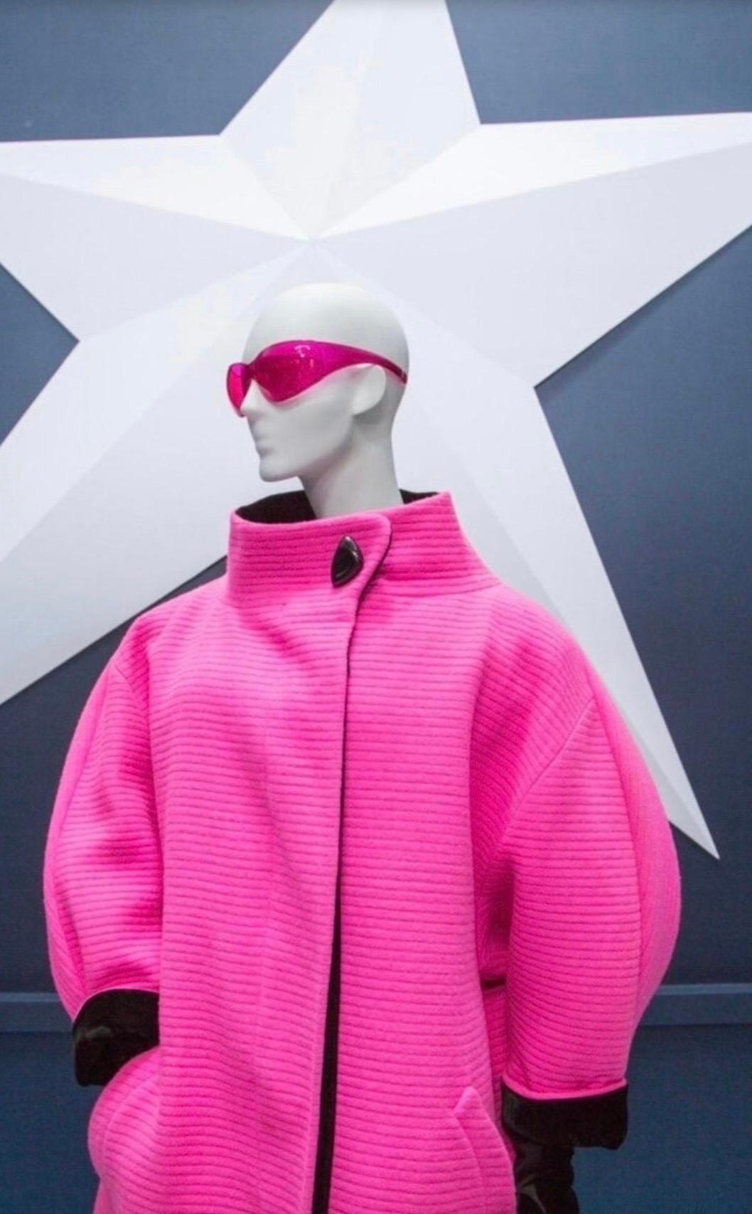 Crea una dichiarazione con questo cappotto avanguardista in lana di Thierry Mugler dell'Autunno/Inverno 1990. Questo rarissimo cappotto rosa fucsia caldo vanta un design futuristico con un ampio collo a imbuto che crea un sorprendente effetto