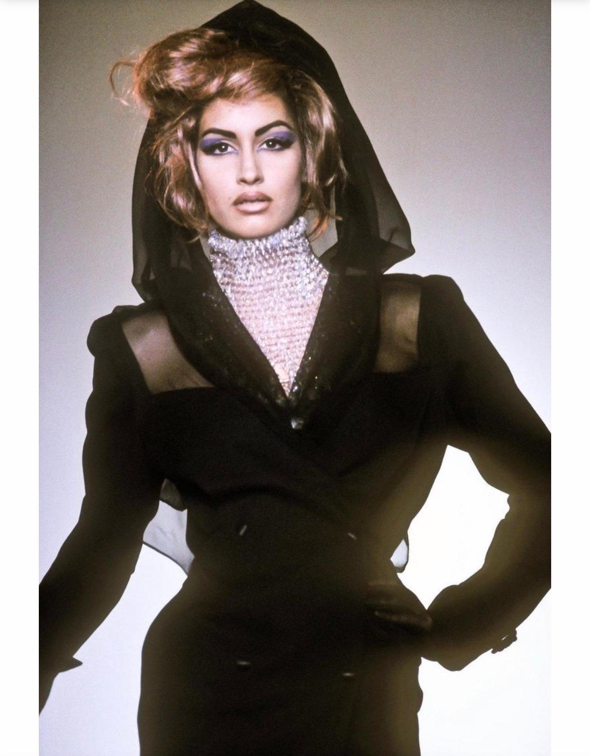 Dalla collezione A. Winter 1991 di Thierry Mugler, questo sorprendente tailleur pantalone nero all'avanguardia è caratterizzato da un blazer doppiopetto dal taglio deciso, arricchito da inserti trasparenti sulle spalle e sulla schiena. Come visto su
