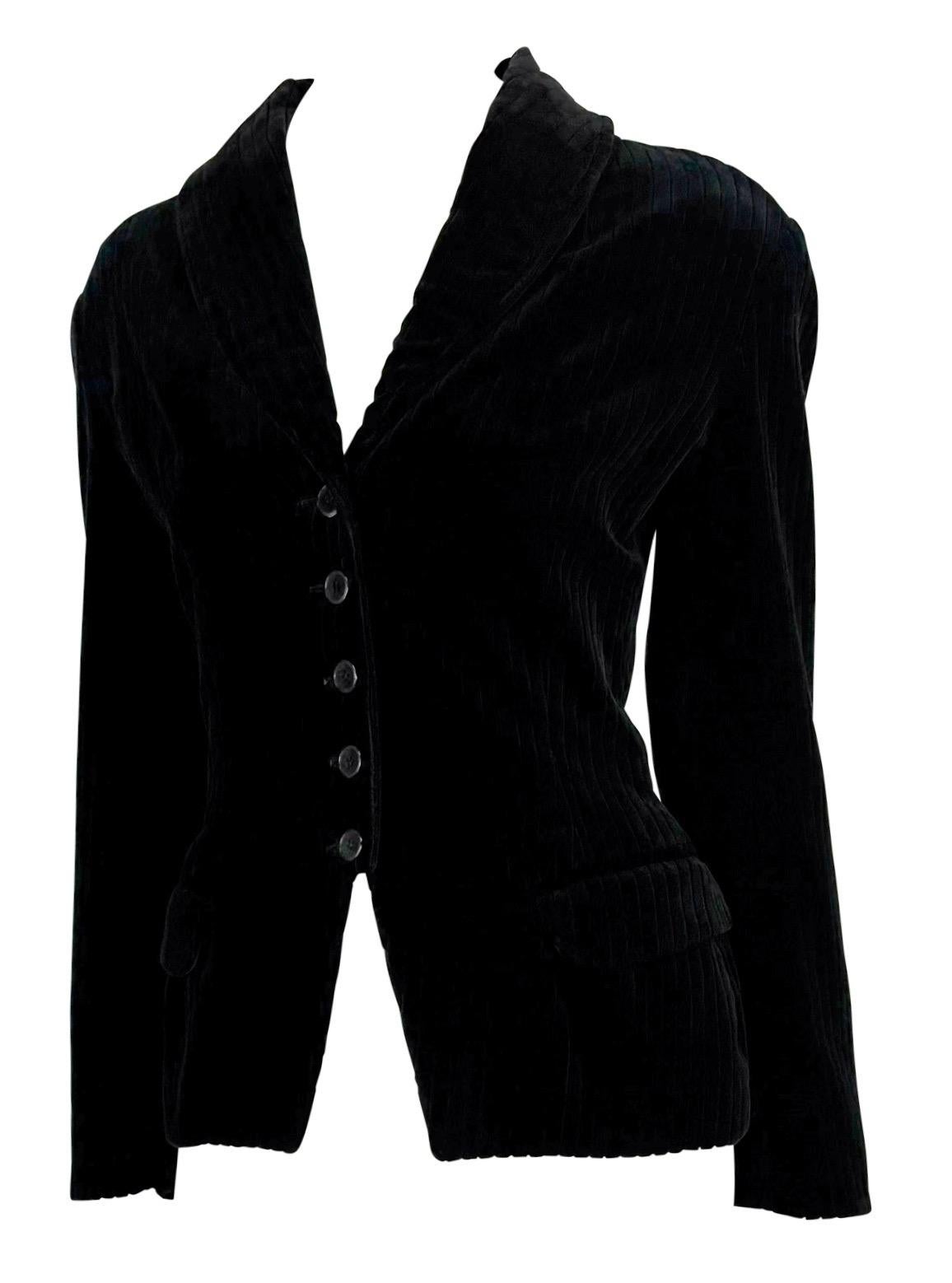 Dalla collezione Autunno/Inverno 1992, questo blazer Alaïa è realizzato in velluto nero a coste con una raffinata trama a canali. Il design sartoriale è caratterizzato da una silhouette scultorea con colletto a scialle, chiusura a monopetto con