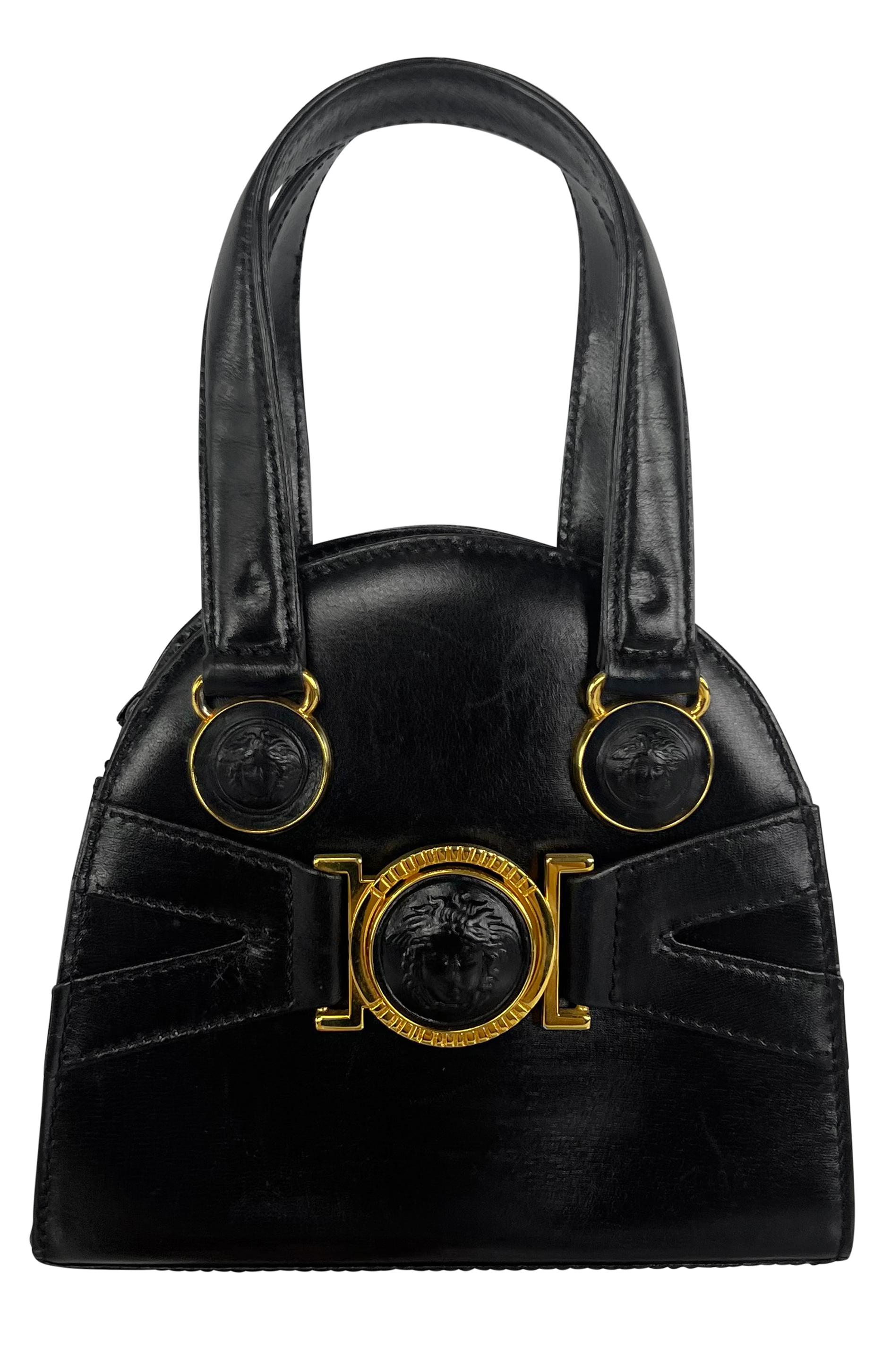 This Gianni Versace black leather mini bag from the Fall/Winter 1992 collection features signature bondage straps and gold-tone Medusa hardware. The bag comes with dual top handles and a removable crossbody strap, offering versatile carrying