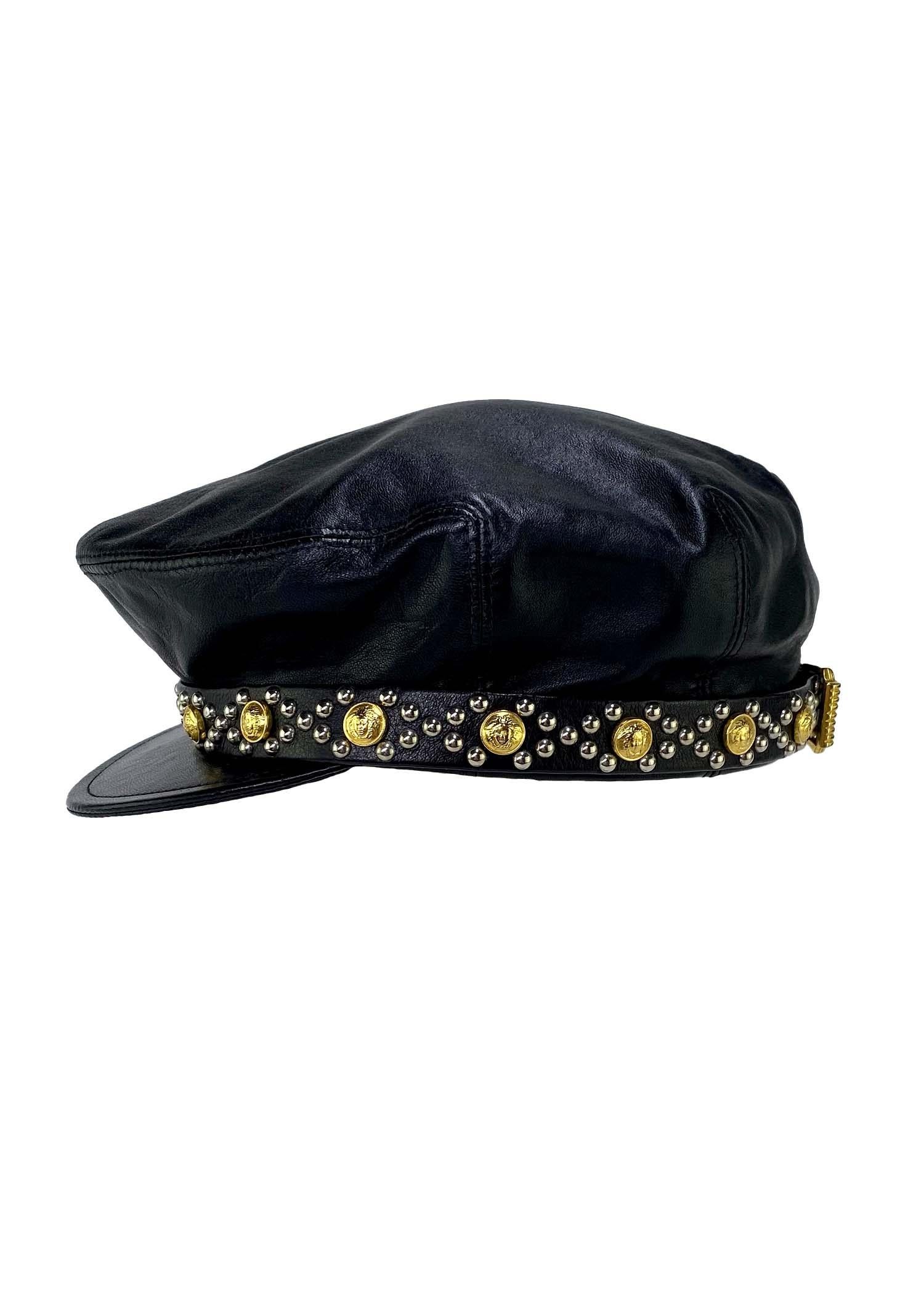 TheRealList presents: a rare leather hat designed by Gianni Versace for his Fall/Winter 1993 collection. This piece is constructed in supple black leather and features a small brim belt band. The silver studs surround gold medusa medallions in a
