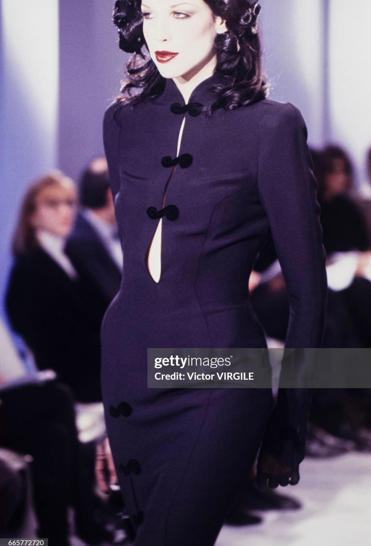 This fabulous black long sleeve ankle length dress was designed by Manfred Mugler for his Fall/Winter 1993 collection. A piece of Mugler's runway history, this ultra chic ankle length dress features a stand up collar, plunging neckline, and slit off